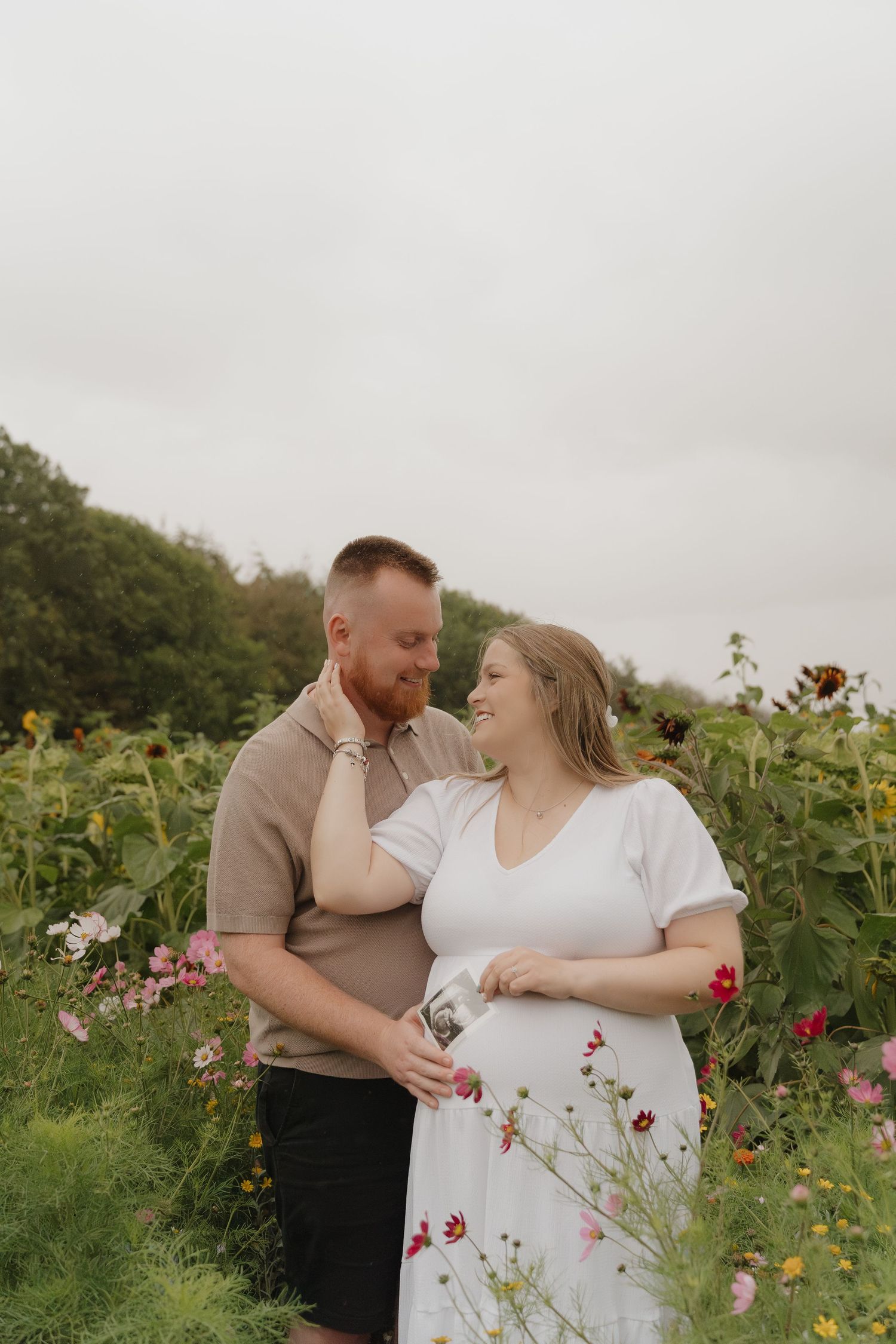 A couple shares an intimate moment in a blooming wildflower field on an overcast day.