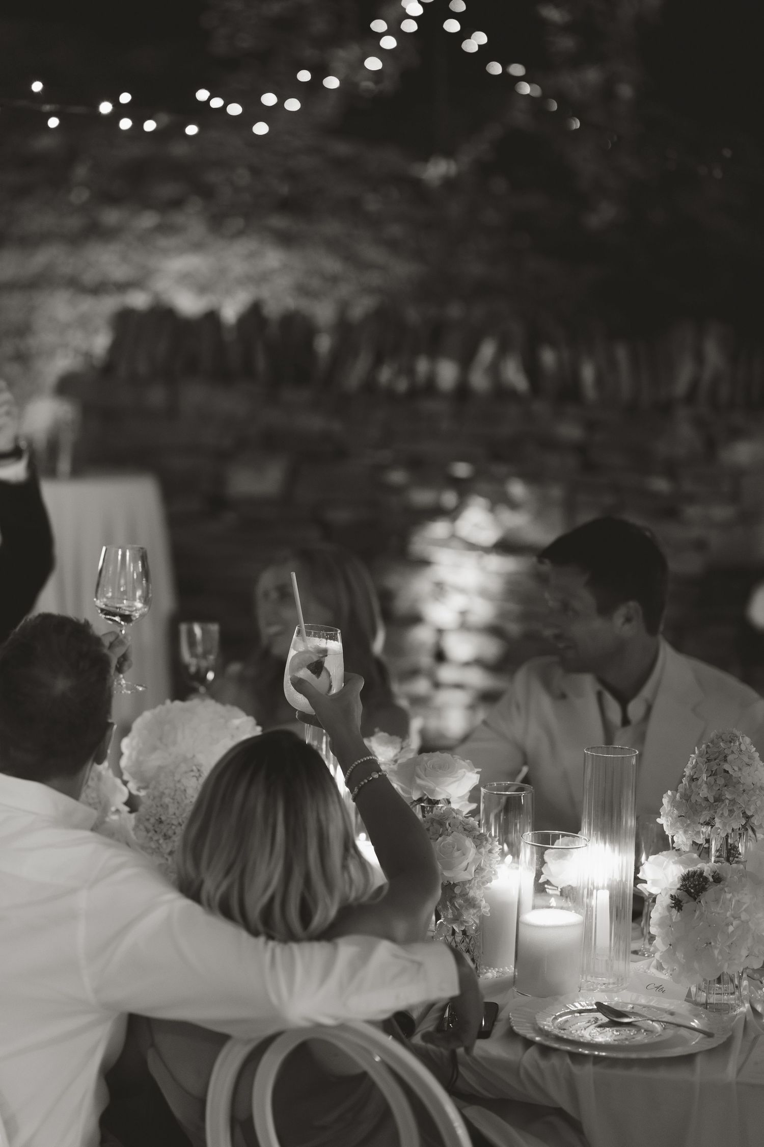 Black and white wedding reception toast in candlelit stone venue with guests raising glasses.