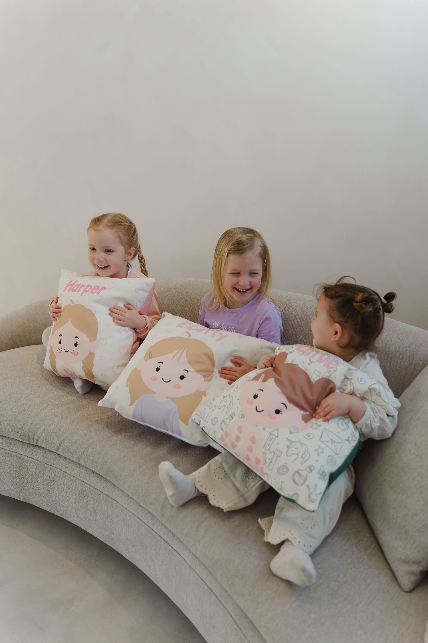 Children playing and laughing together while lounging on a curved gray couch with decorative pillows.