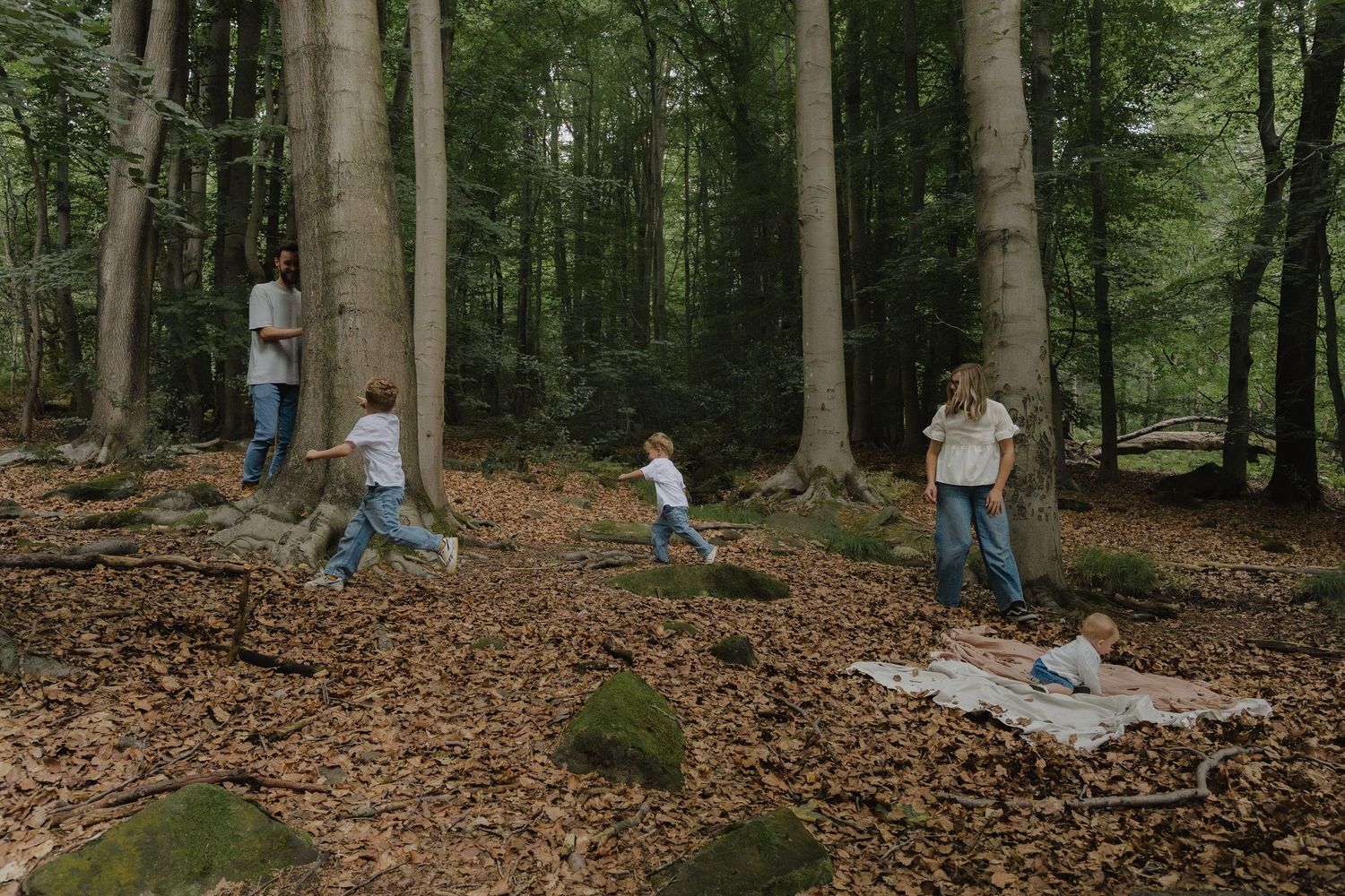 Outdoor family photography in a forrest of fallen autumn leaves and tall trees taken in Derbyshire by Shots by Maz Photography