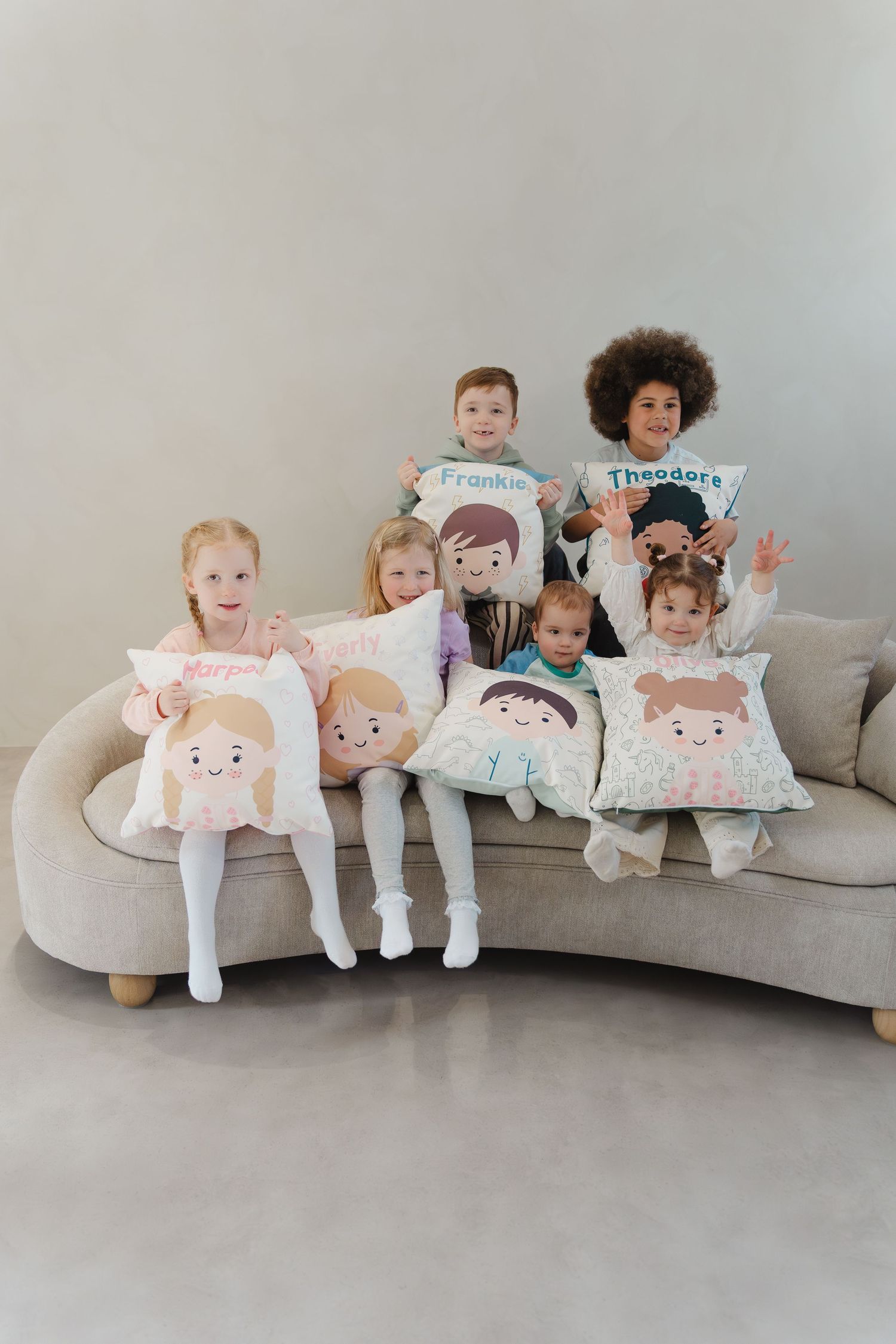A series of decorative throw pillows on a gray couch featuring cute cartoon character designs and faces.