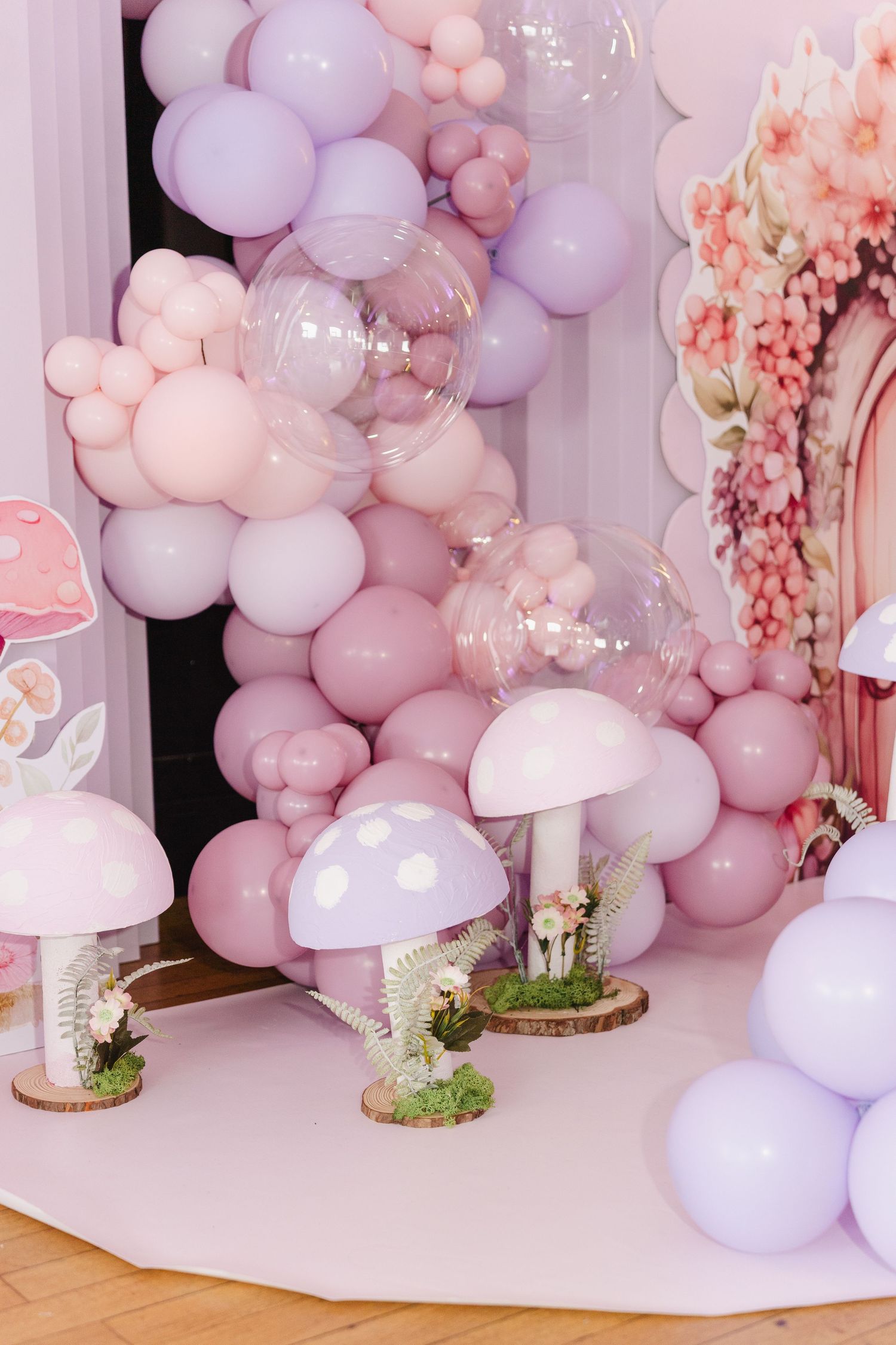 Pink and purple balloon garland with mushroom decorations for a whimsical fairy-themed birthday party setup.