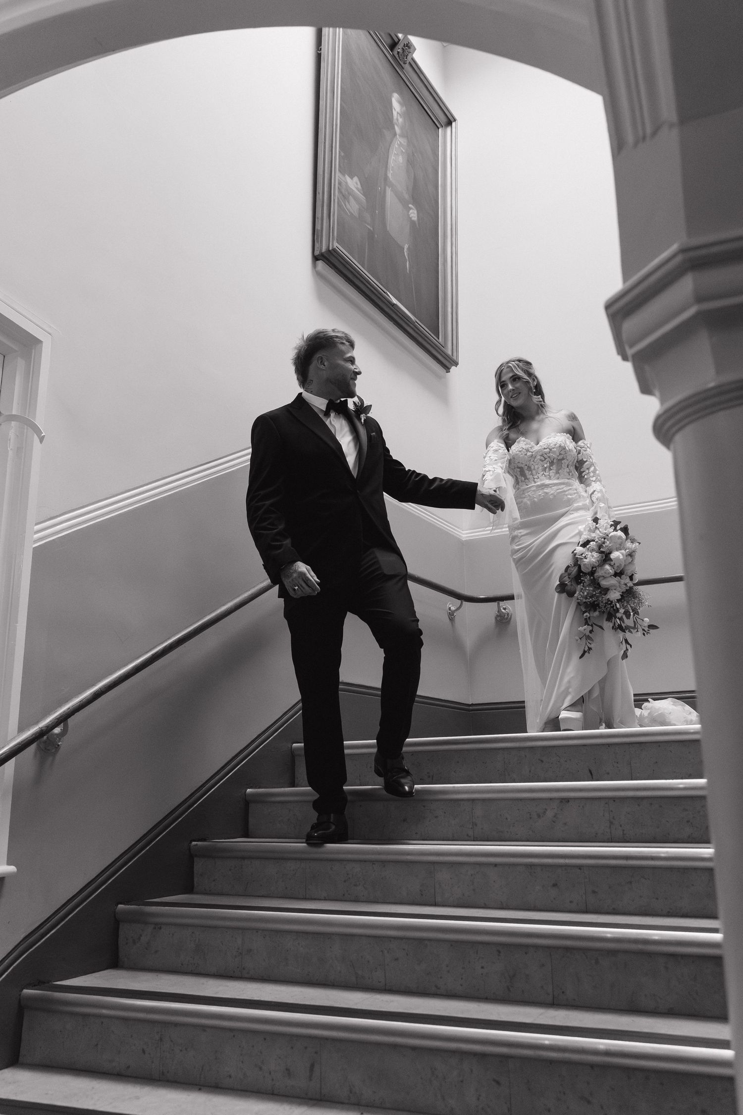 Registry office wedding photographer Derbyshire. Black and white photo showing a couple descending grand staircase in wedding attire.