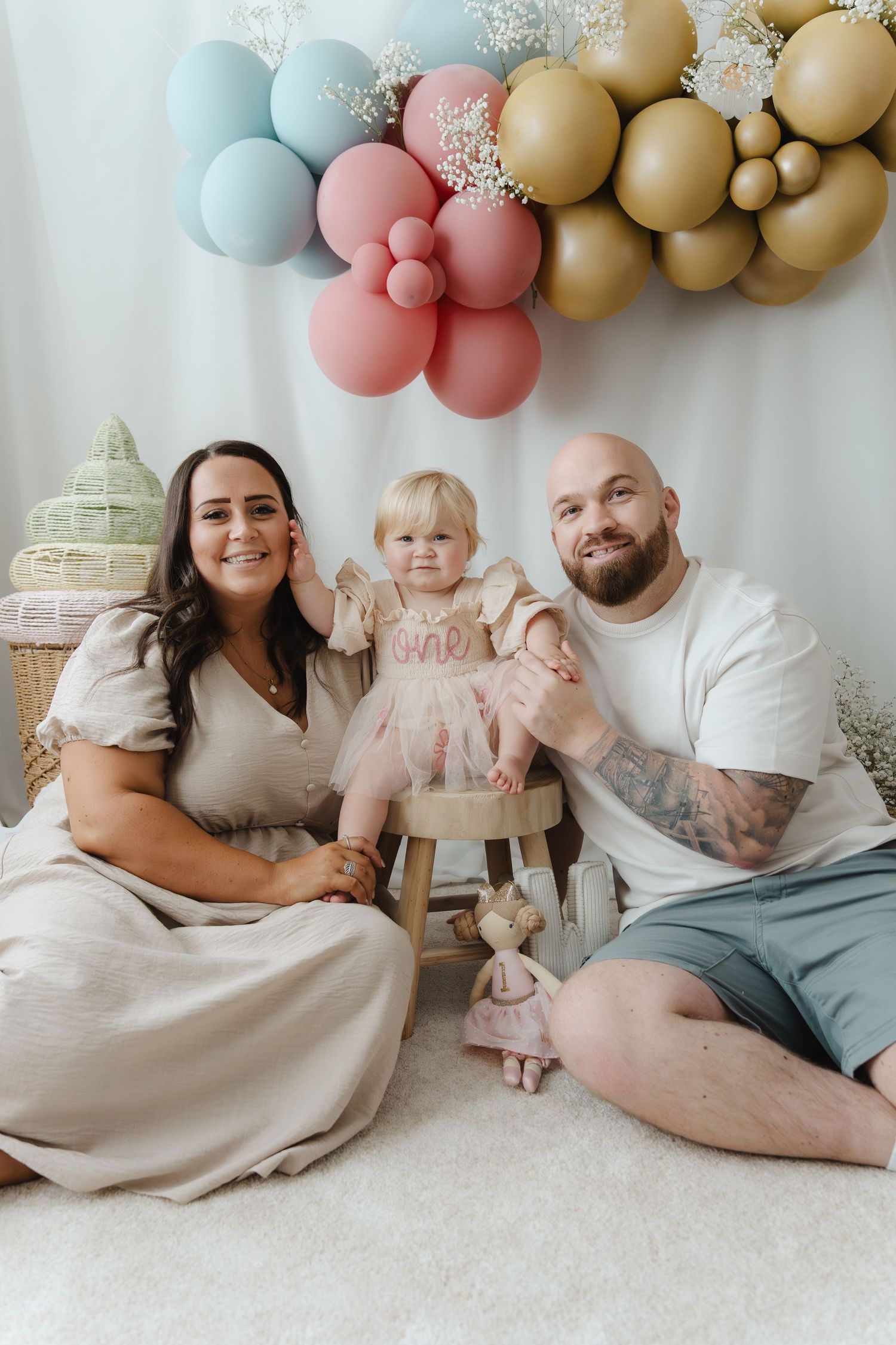 A family sits together on a carpet under pastel balloon decorations for a special celebration.