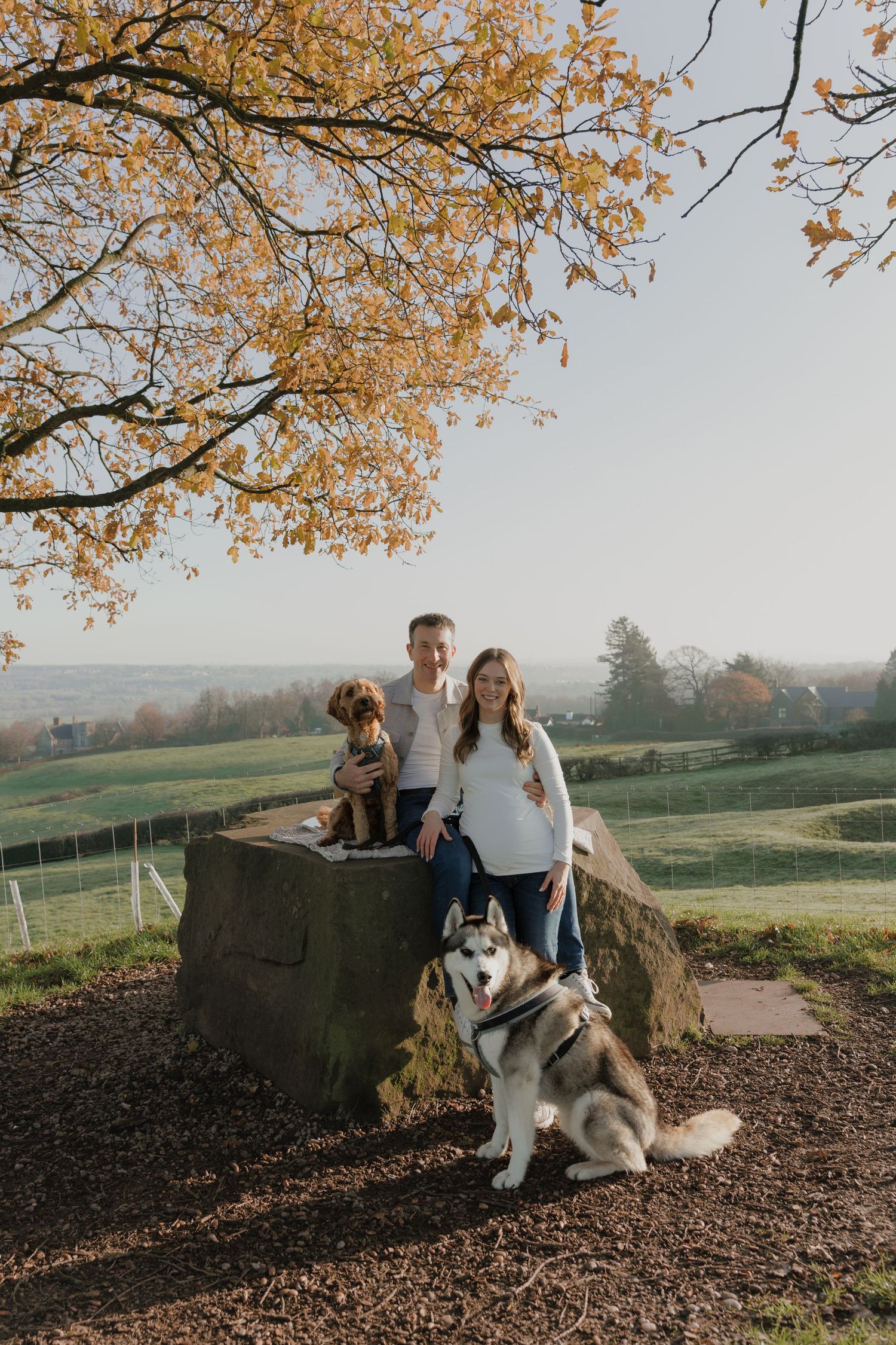 Couple photographed with husky dog under autumn tree branches in countryside setting at sunset in Derbyshire captured by Shots by Maz.