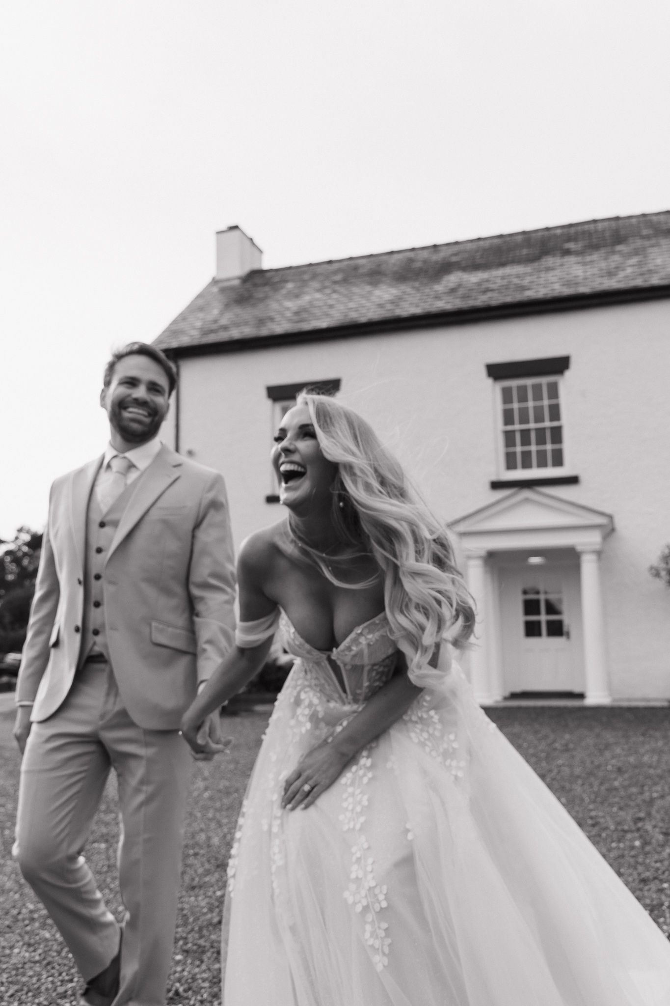 A happy couple in wedding attire laugh together in black and white photos against a white building exterior.