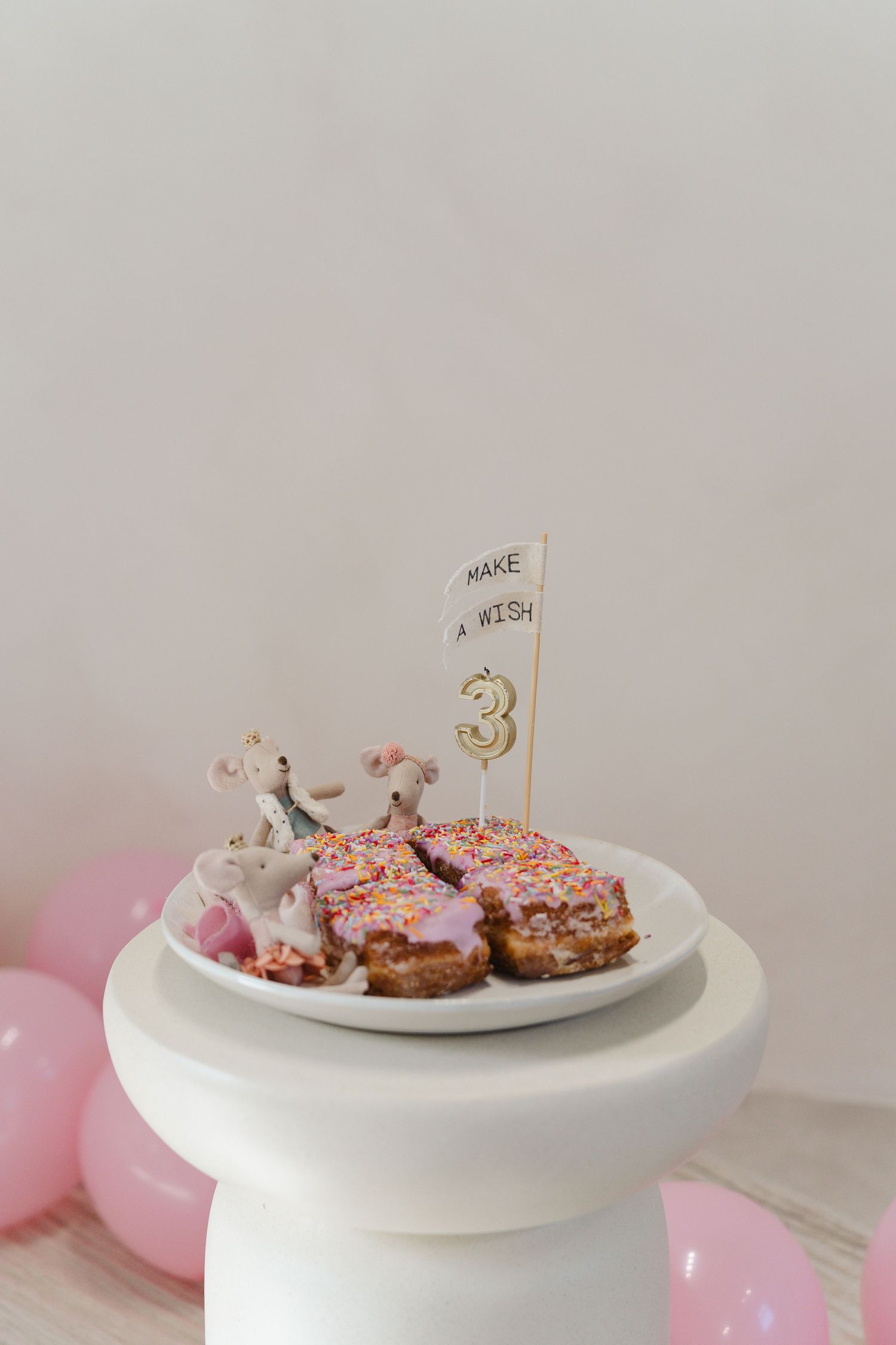 Birthday decorations with pink balloons and a number 3 cake topper on a white pedestal.