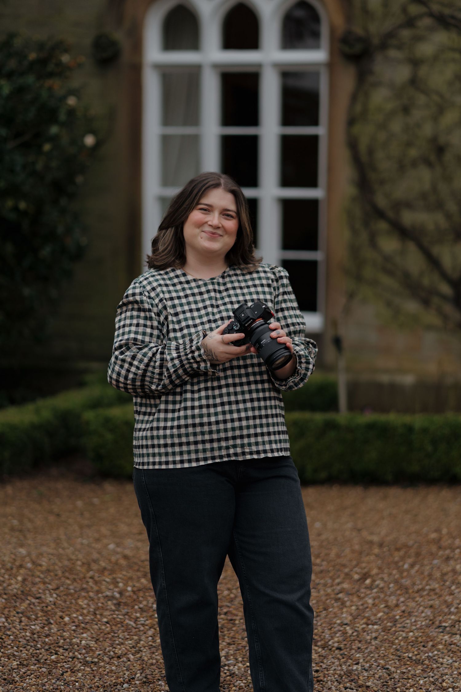 Derbyshire family photographer stands smiling while holding a professional camera outside Dunston Hall in Chesterfield