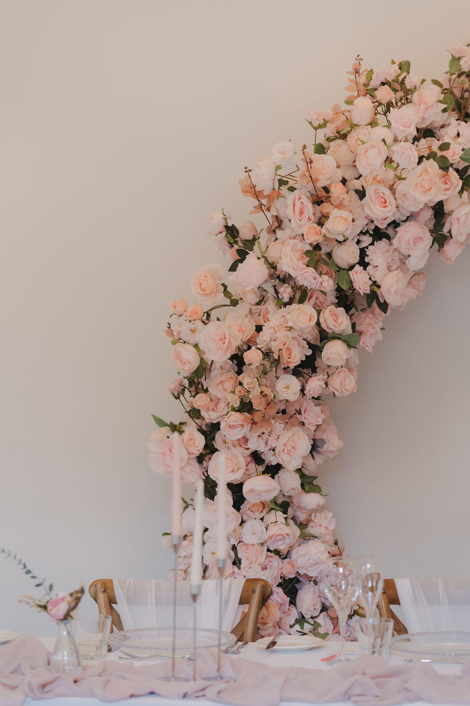Elegant pink floral arrangements cascade over clear glass vases at a wedding reception table setup.
