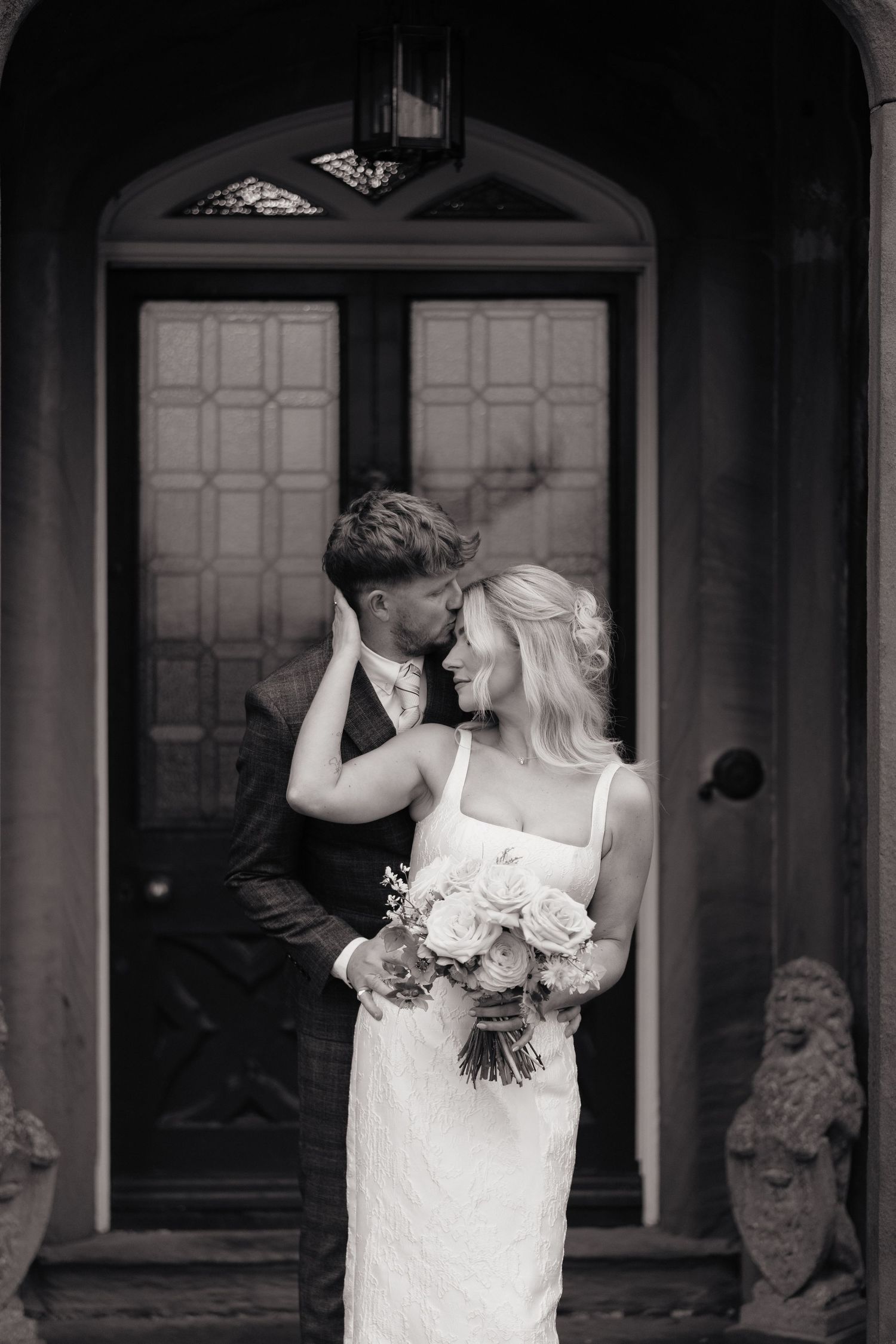 A romantic black and white wedding portrait showing tender moments between a couple in front of an ornate doorway in Derbyshire.