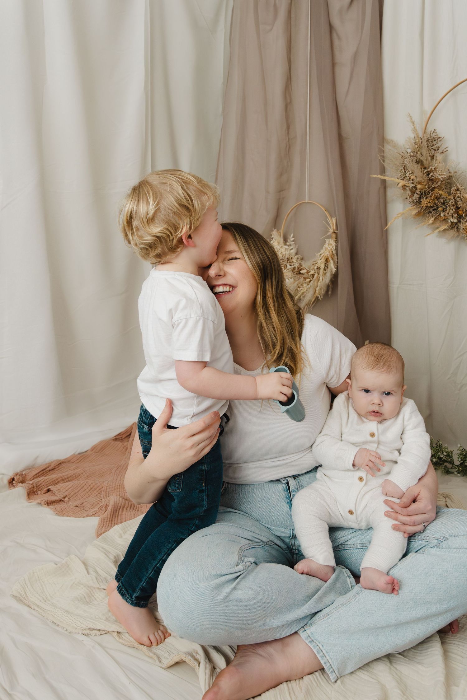 A tender family moment on a cozy blanket with neutral decor and dried flowers in the background.