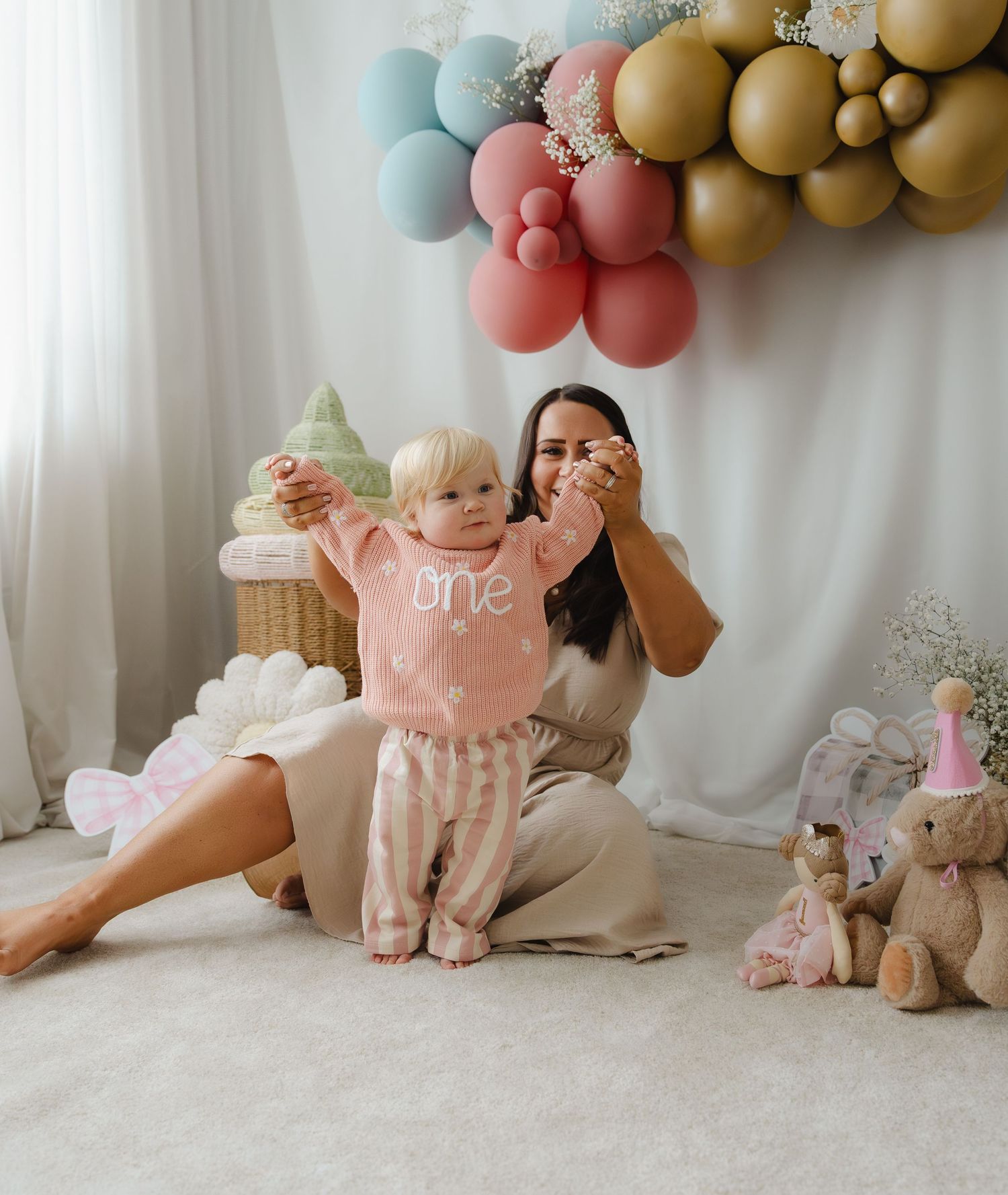 Soft pastel balloon arch and teddy bear decorations create a dreamy first birthday photo session setup.