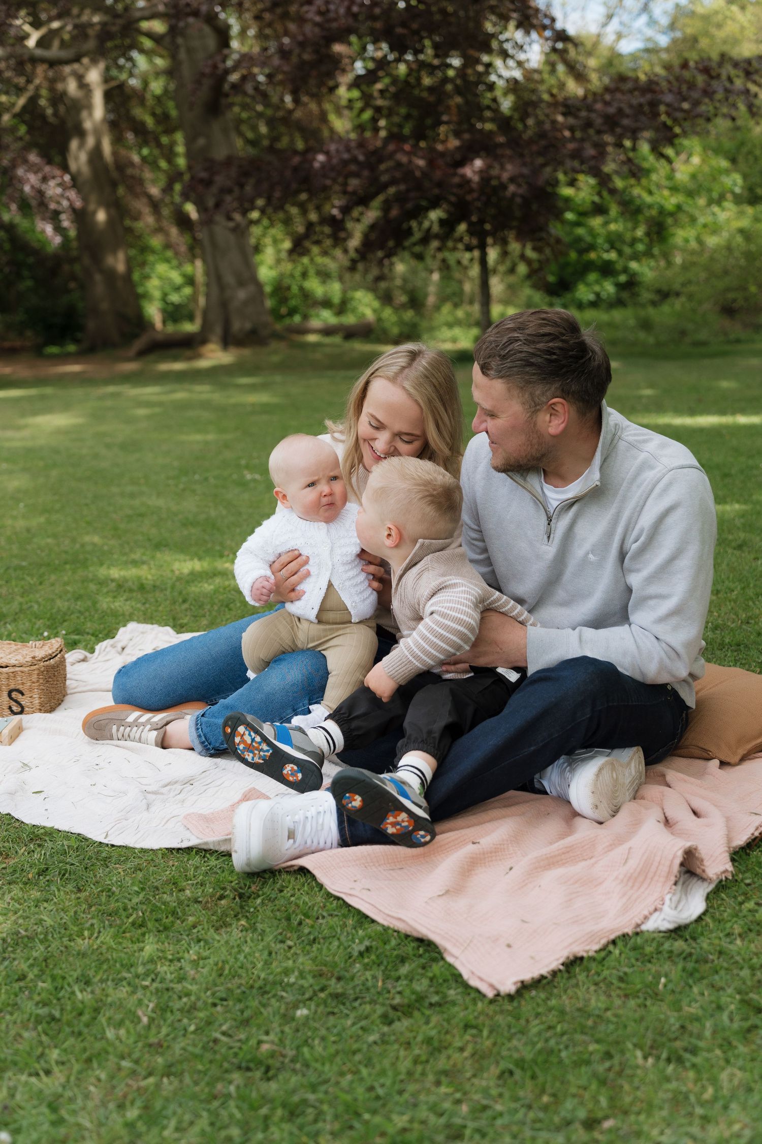 Happy family of four enjoying a picnic on a blanket in a lush green park on a sunny day.