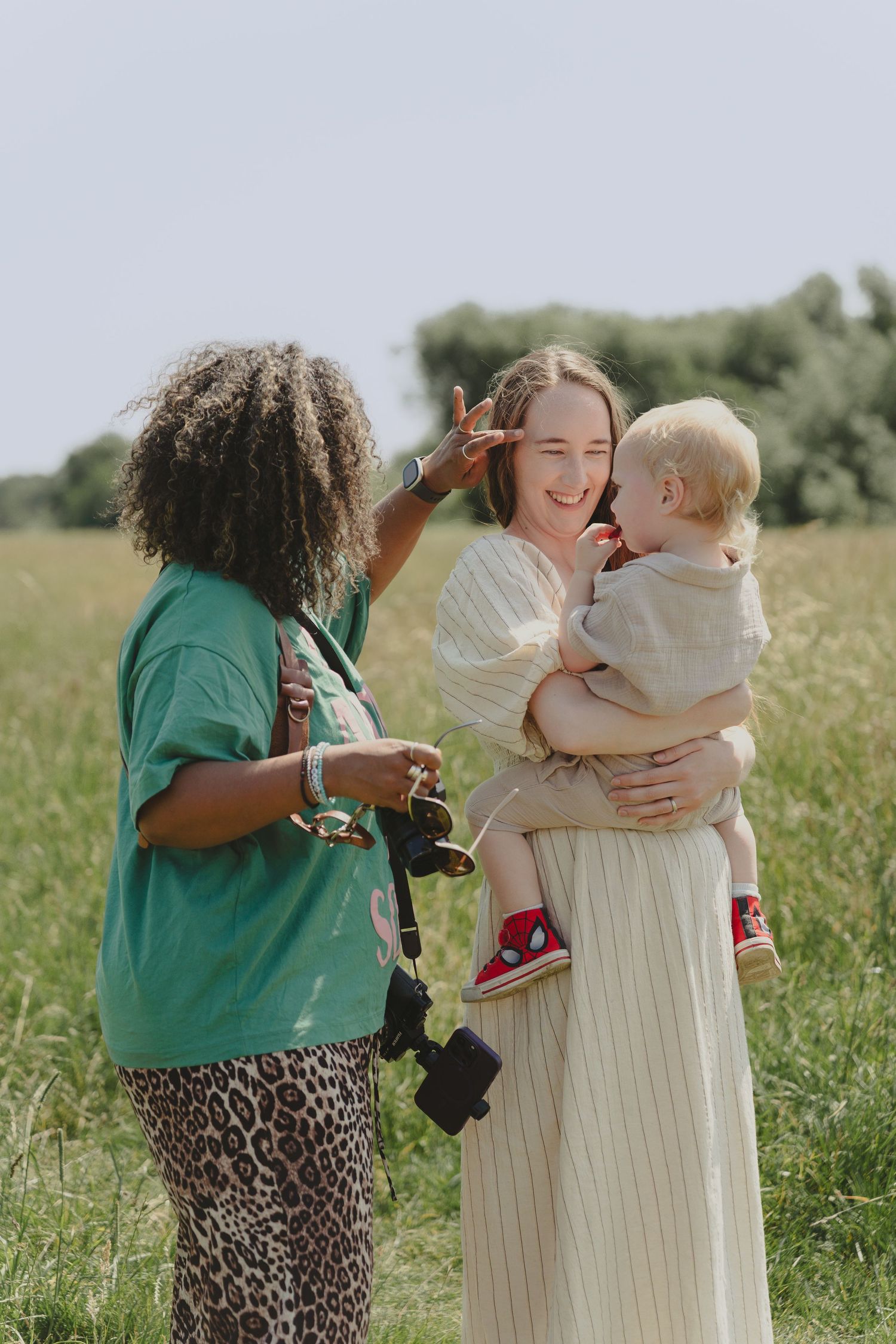 Photographer in green shirt and leopard print pants interacts with subjects during outdoor photo session in a field.