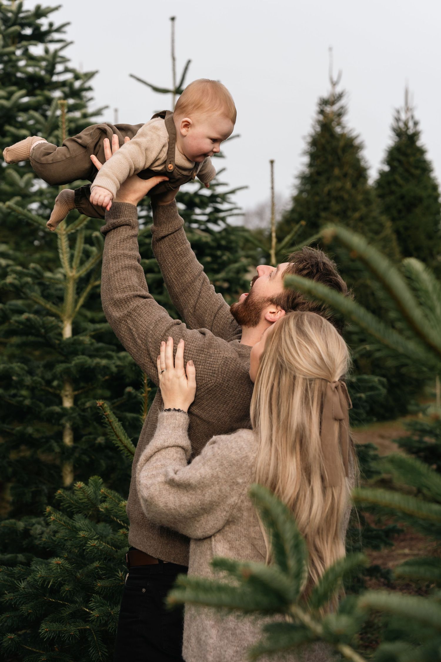 A joyful family moment captured among evergreen trees at a Christmas tree farm.