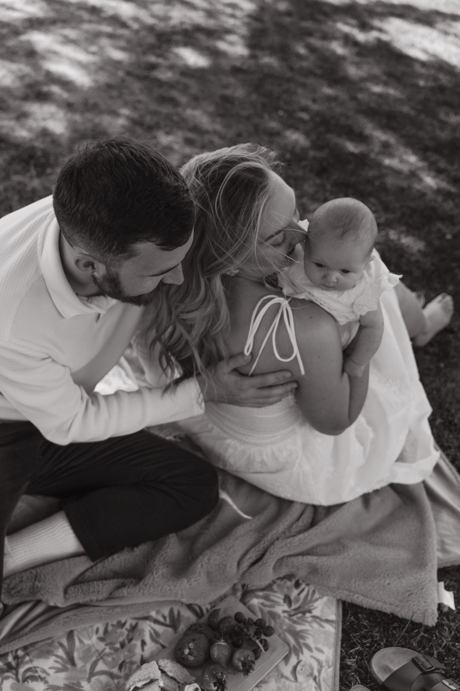 Black and white photo series showing tender moments between a couple laying on a blanket outdoors in dappled sunlight.