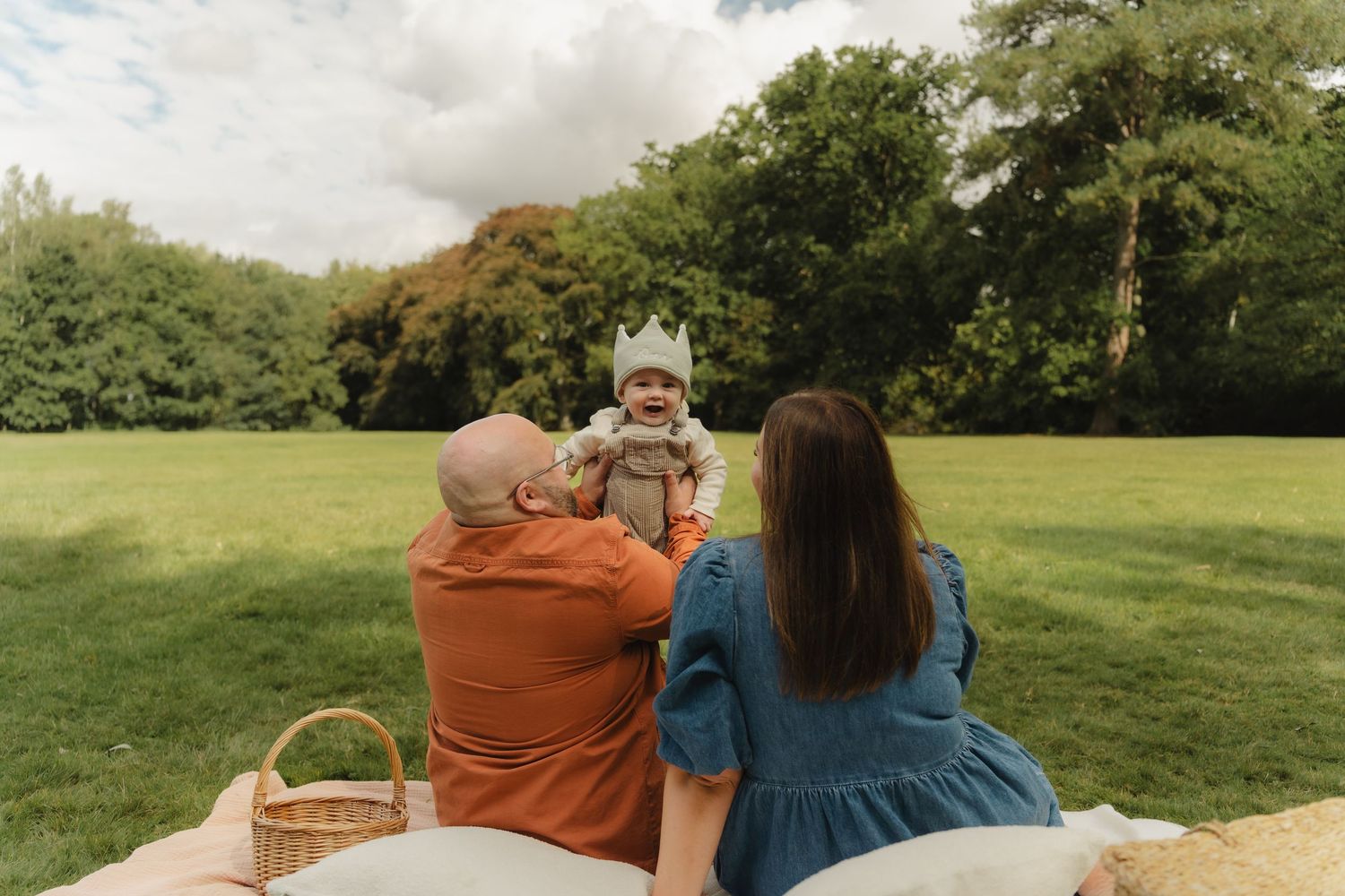 A couple sits on a picnic blanket enjoying a scenic view of a green meadow on a summer afternoon.