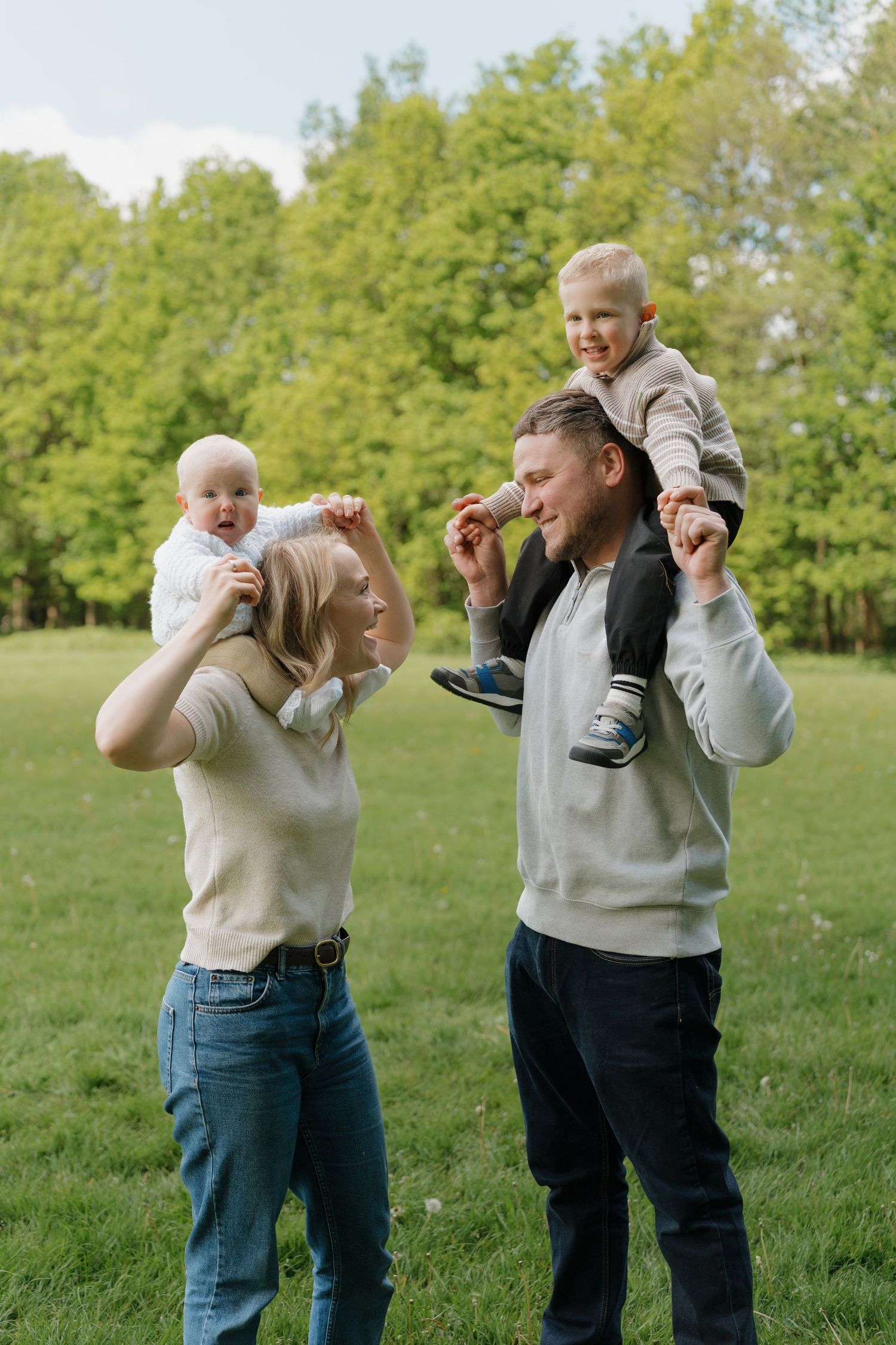 Happy family with two young children on their shoulders enjoying a sunny day in a lush green park.