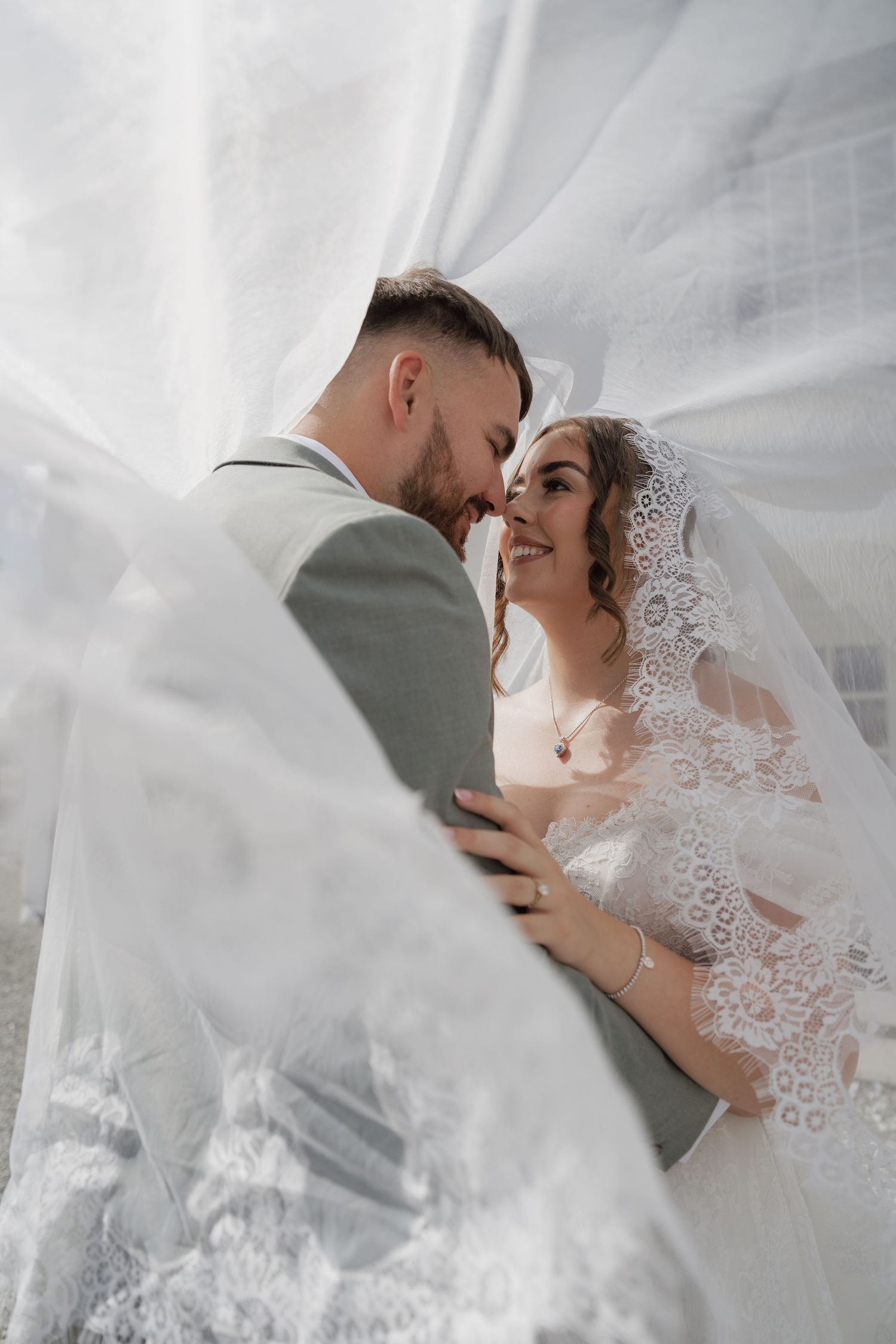 A bride and groom share a romantic moment under a flowing white veil on their wedding day.