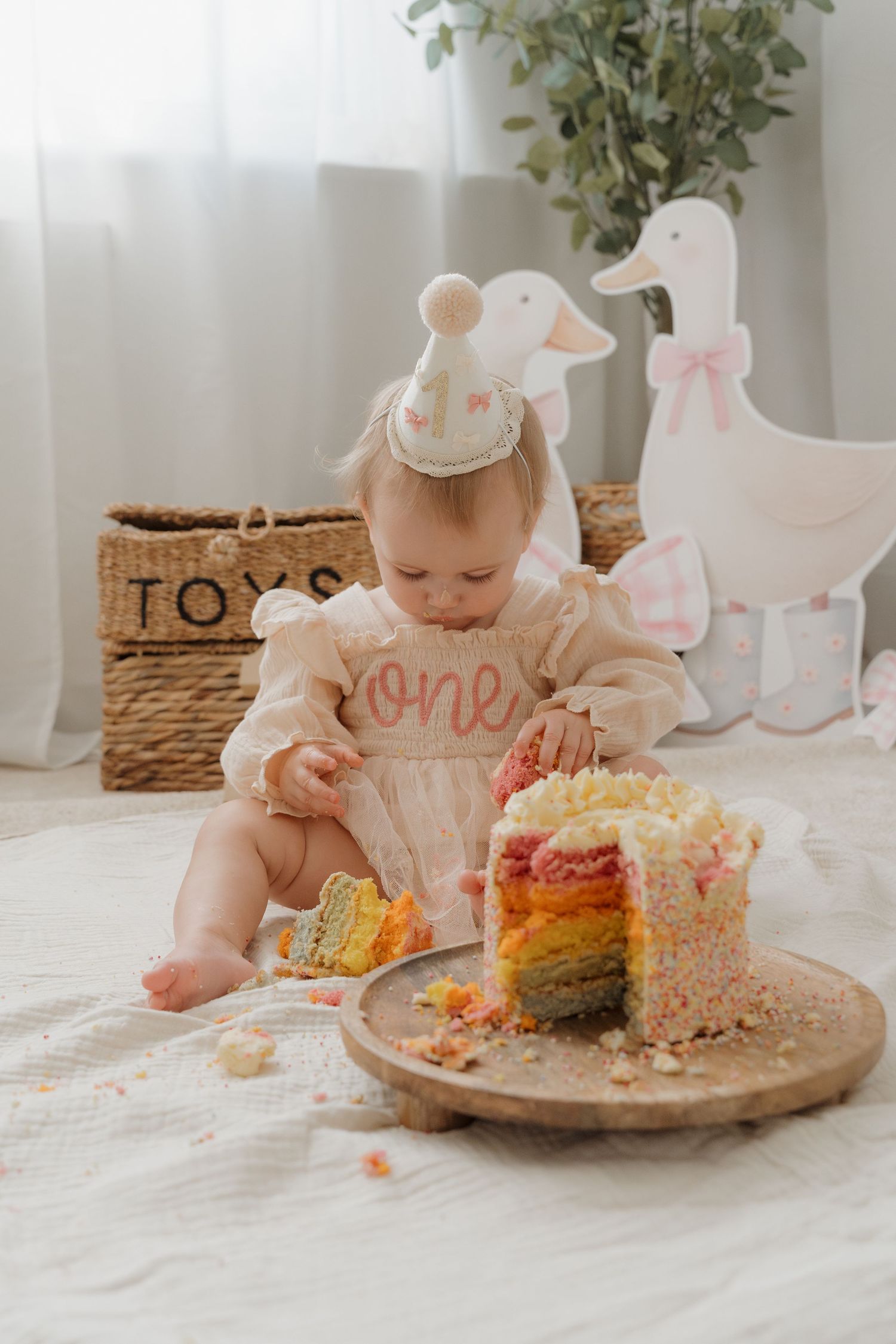 Rainbow layered cake smash session featuring soft pastel colors and white decorative elements on a neutral background.