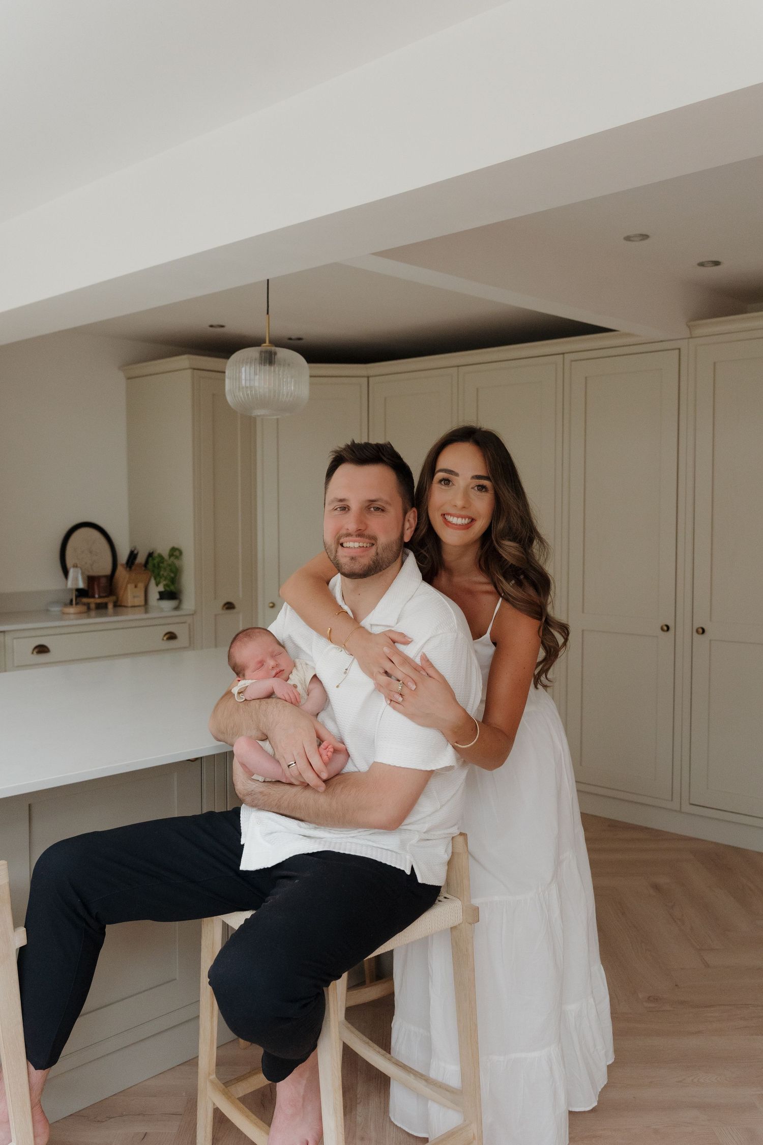 A couple playfully dances and embraces in a bright modern kitchen with white cabinets and hardwood floors.