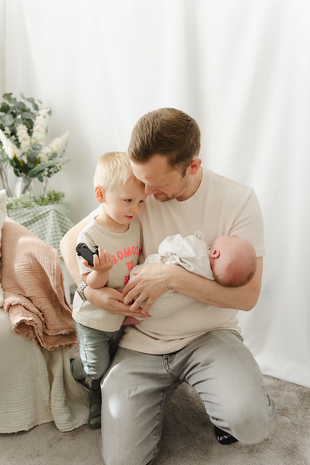 A parent and young child share tender moments together in a bright white studio setting with potted plants in background.