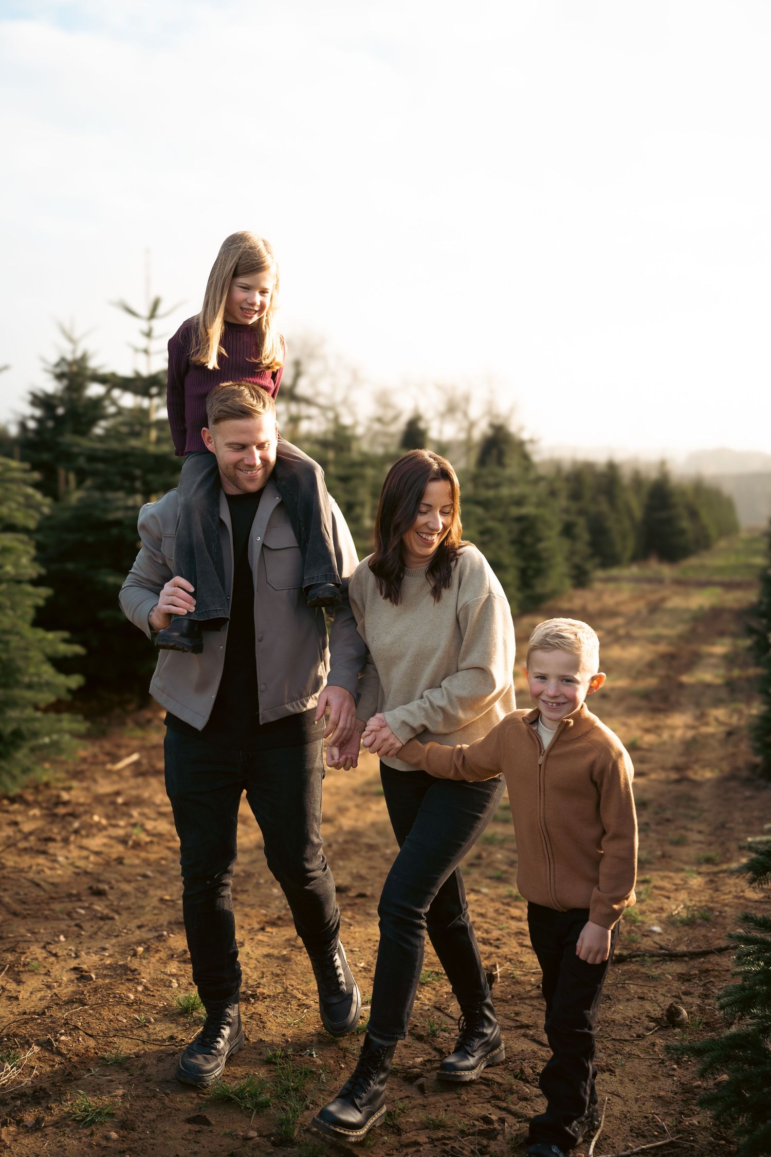 Family enjoying a fun walk together through an evergreen tree farm at sunset on a fall afternoon.
