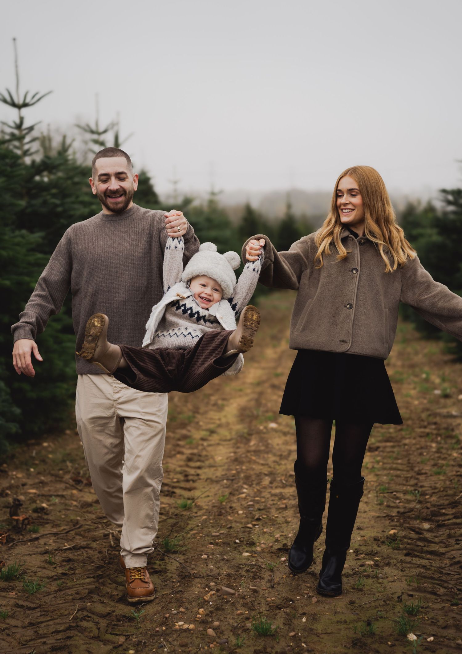 Couple walking and holding hands along a dirt path at a Christmas tree farm on an overcast autumn day.