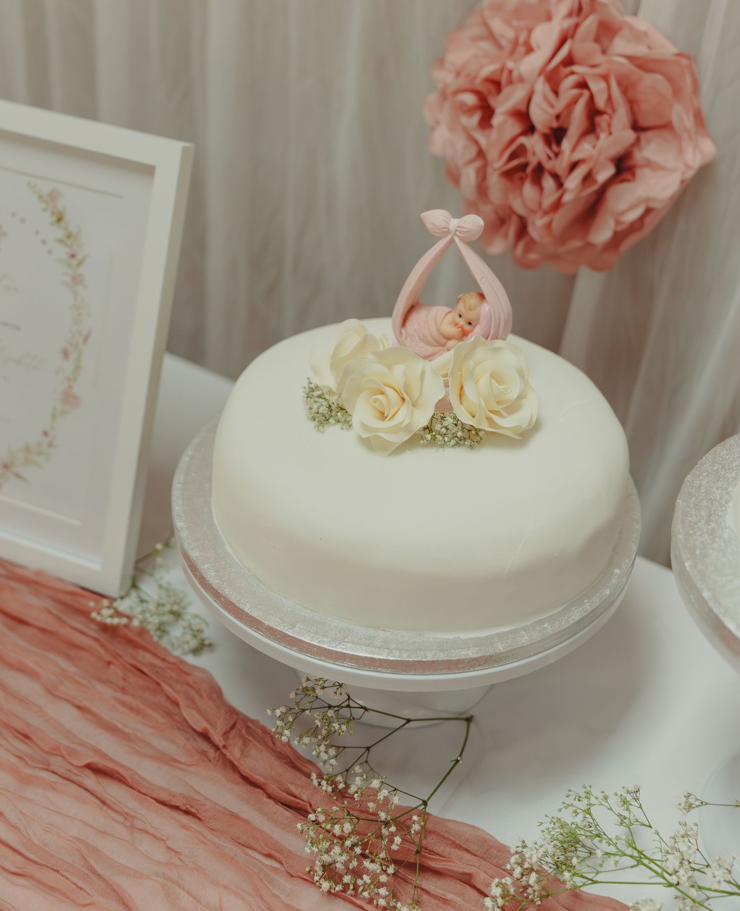 Elegant white wedding cake decorated with delicate coral-colored flowers and baby's breath on a white pedestal stand.