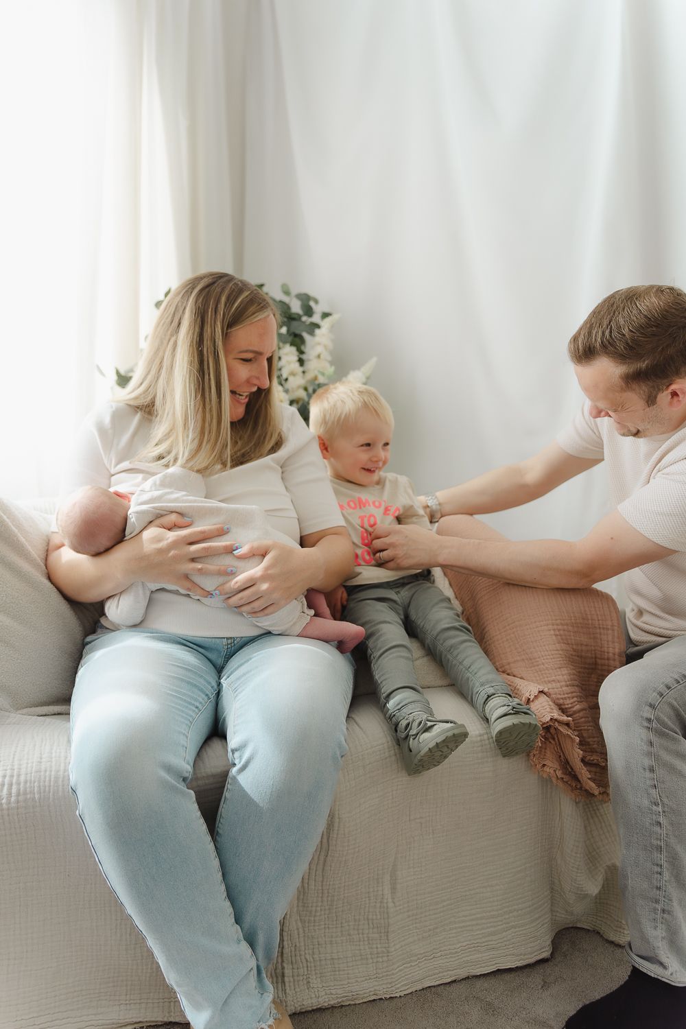 Family relaxes together on a light gray couch sharing playful moments.