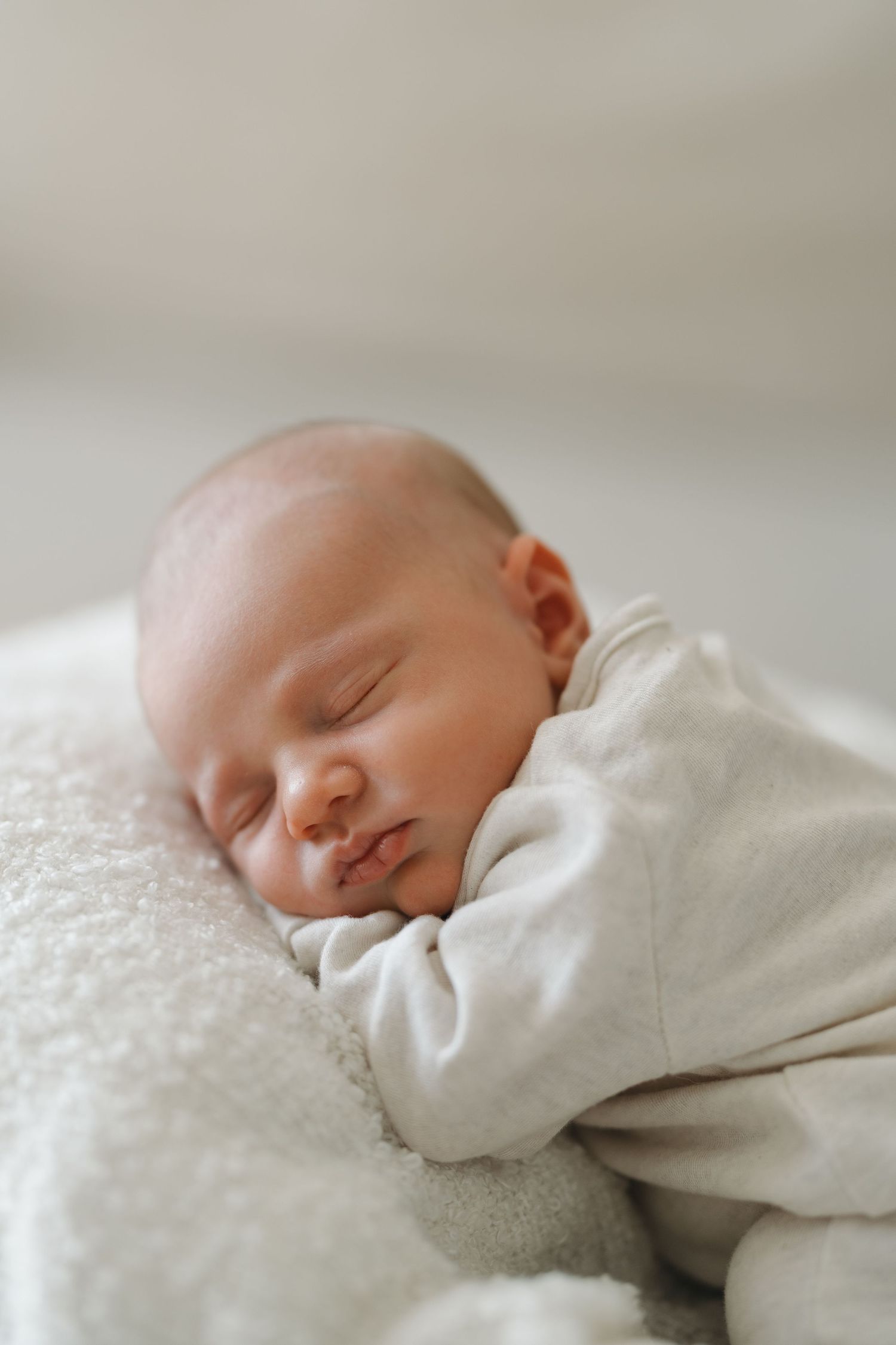 A peaceful newborn baby sleeping soundly on a soft white blanket, wearing a cozy white outfit.