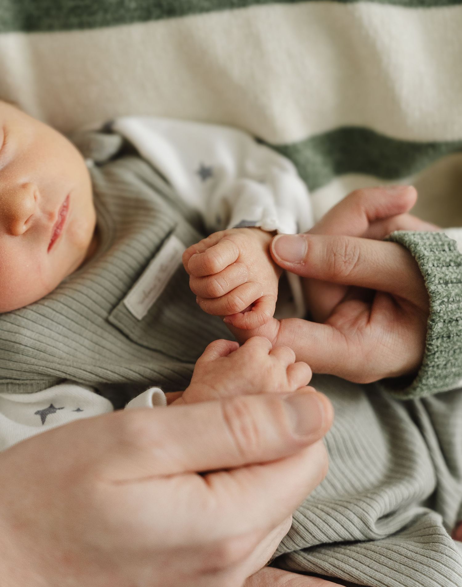 Close-up view of gentle hands holding and caressing a soft gray knitted fabric with delicate care. Documentary newborn photography in Derby