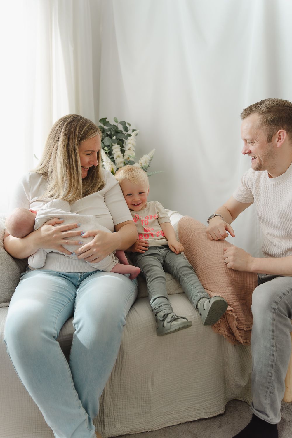 A family shares joyful moments together while sitting on a light gray couch in a bright white room.