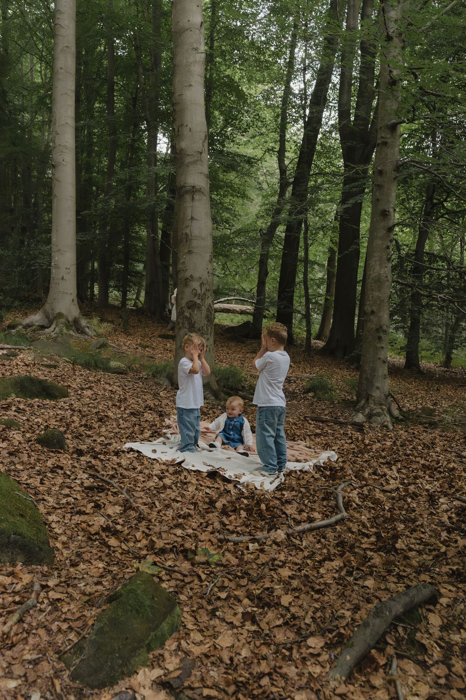 A family plays together in a wooded area covered with fallen autumn leaves.