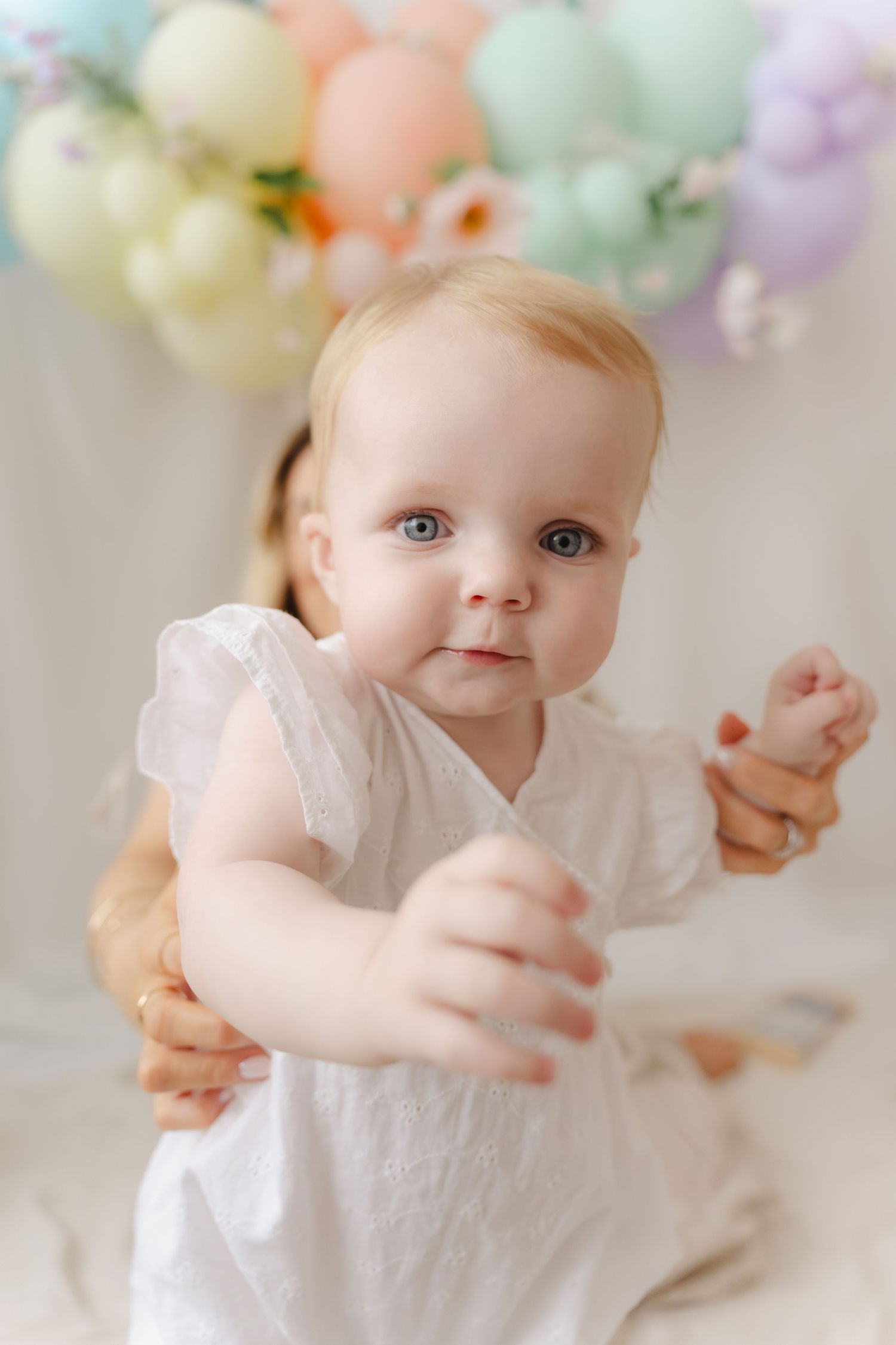 A baby in a white dress poses against a soft pastel floral backdrop in a series of connected photos.