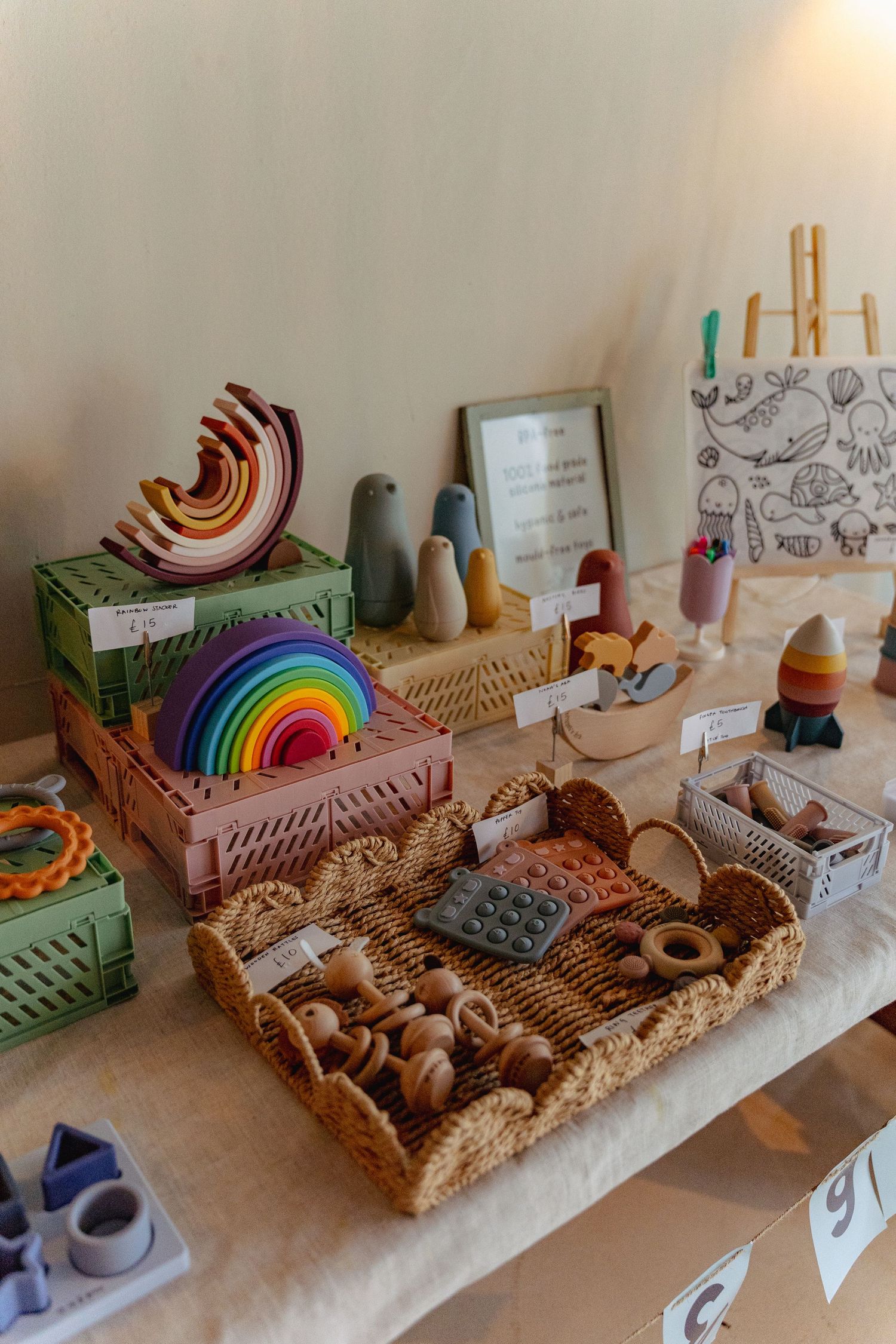 Montessori-style wooden toy shelf displays colorful rainbow arches, natural materials, and educational manipulatives in woven baskets.