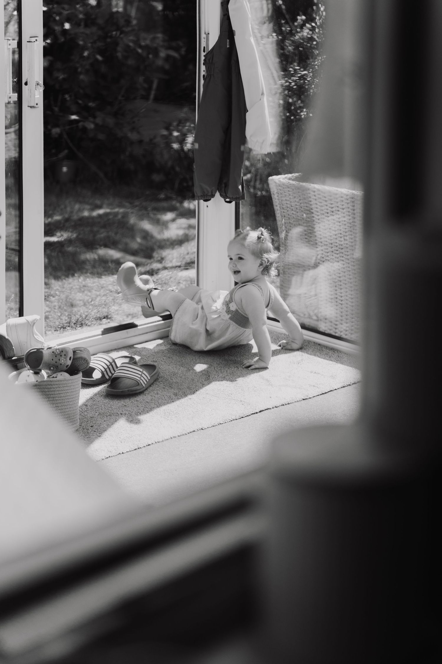 Black and white photo of a happy toddler playing on a rug near an open door leading to a garden.