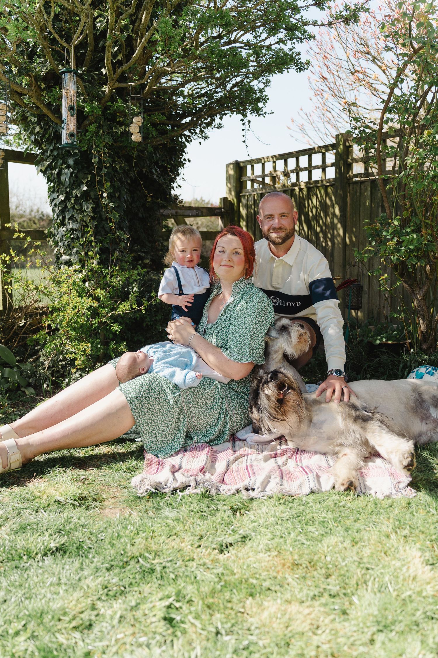 Family relaxing on grass with their Husky dog in backyard on sunny day.