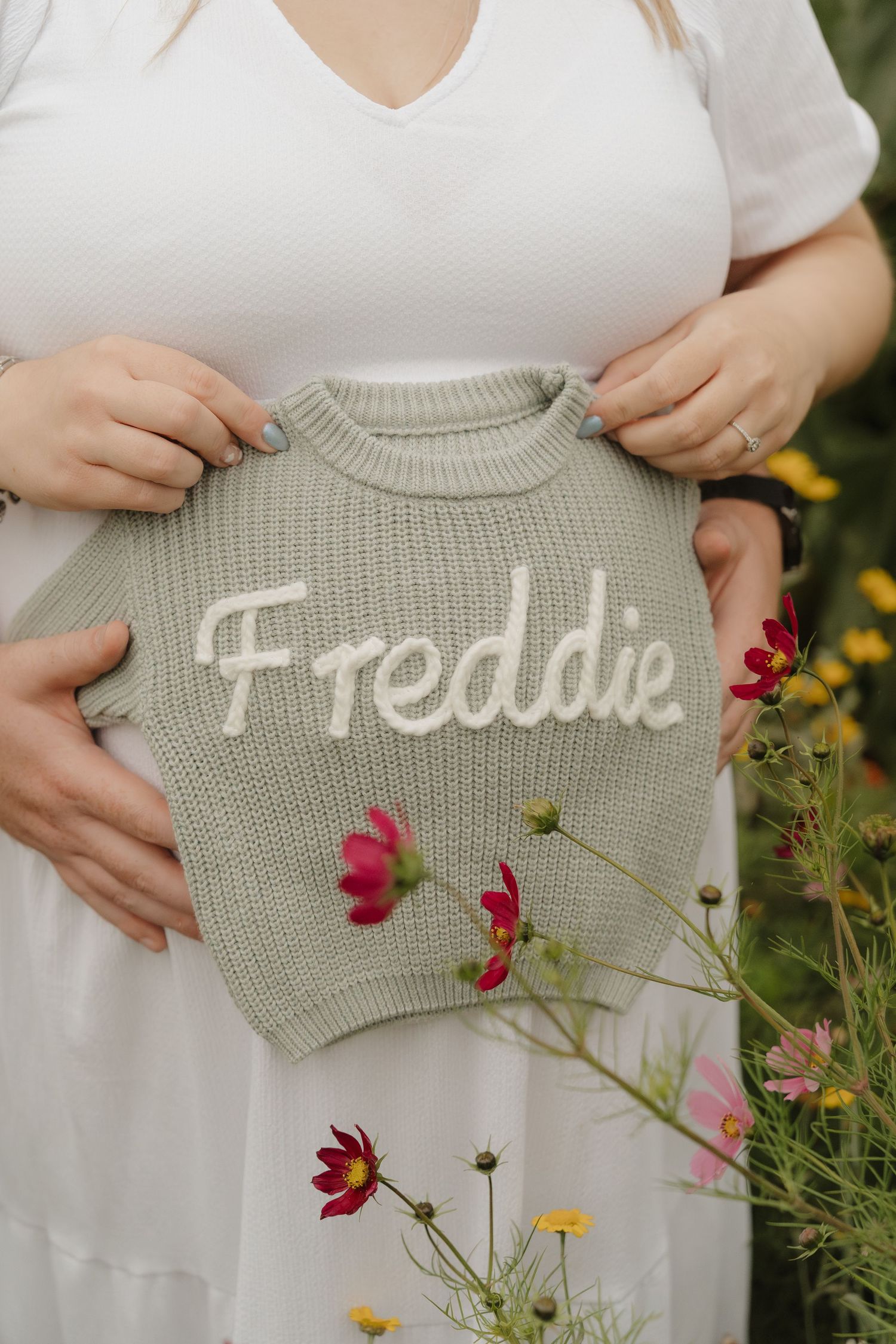 A series of photos showing a sage green sweater with the word 'Freddie' displayed against a backdrop of colorful flowers.