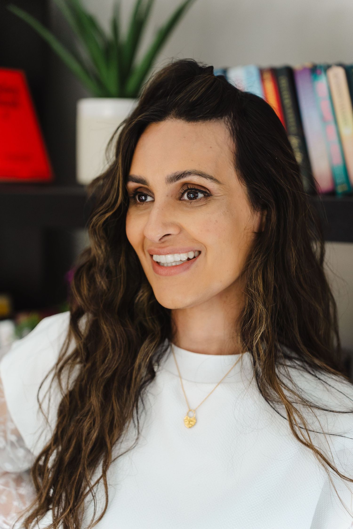 Person wearing a white turtleneck sweater smiles while posing against a bookshelf background.
