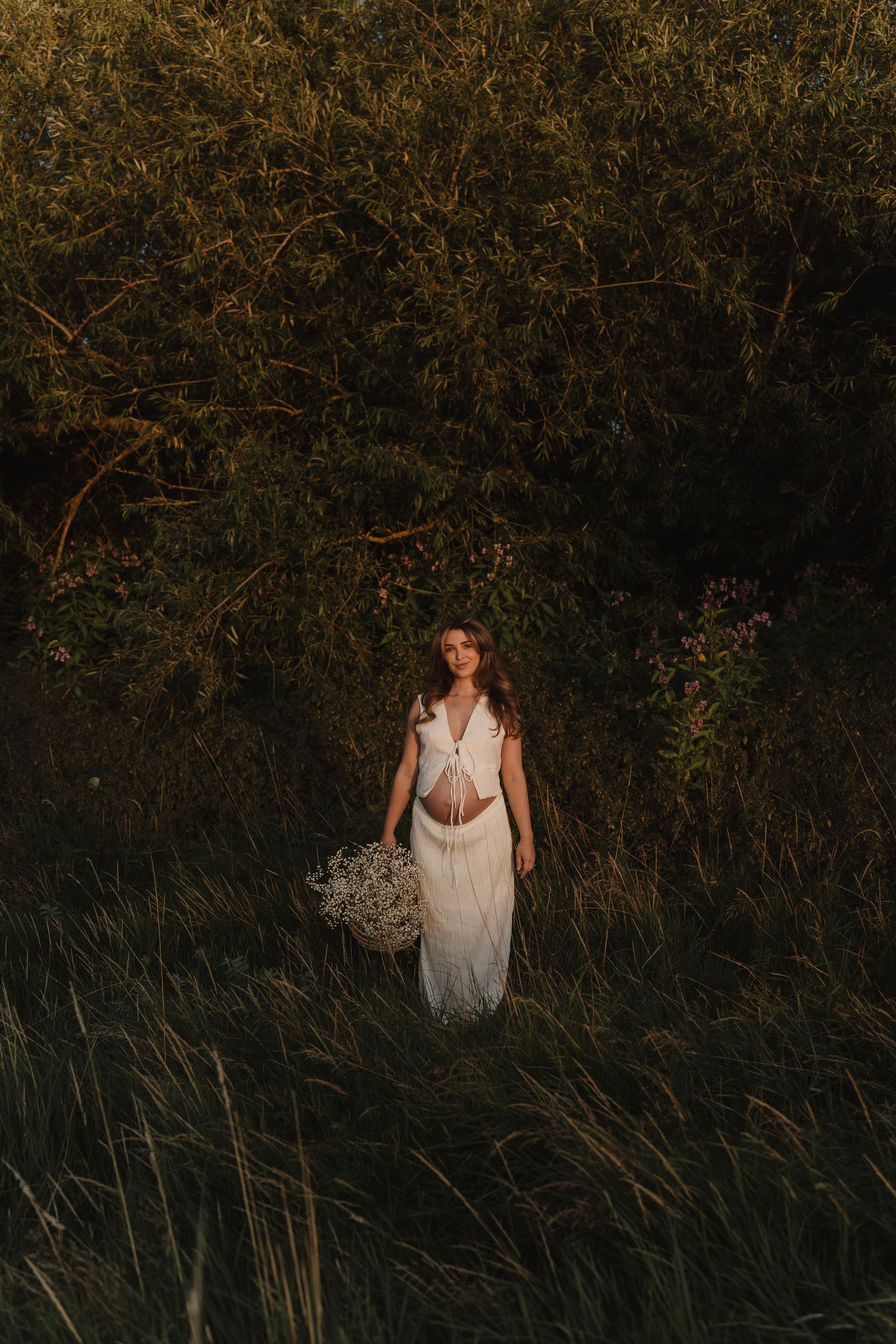 Woman in white dress walking through tall grass at golden hour.