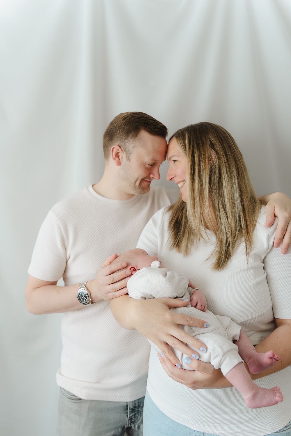 Parents in matching white shirts cradle their infant while sharing intimate family moments.