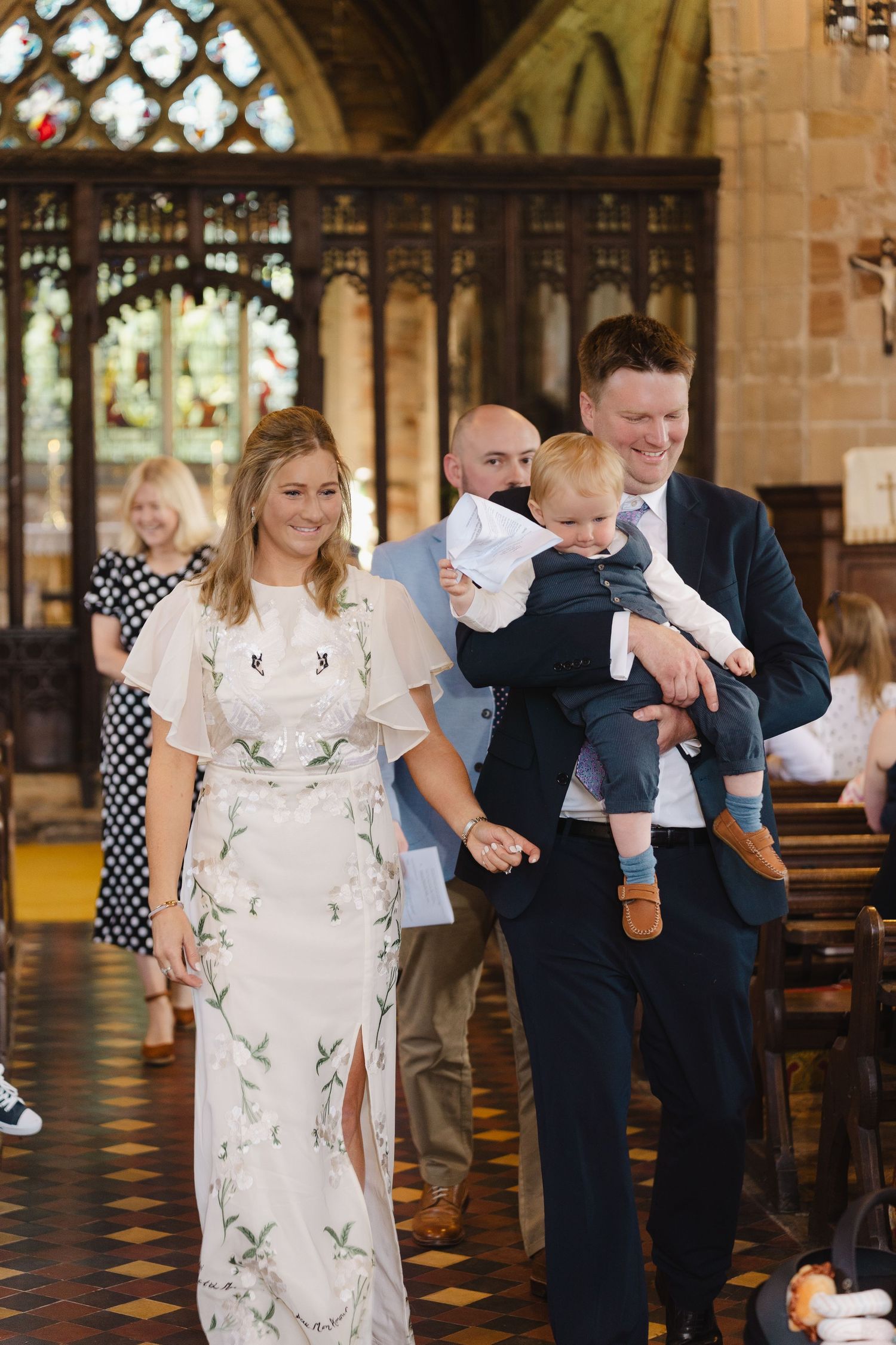 Family walks through a church corridor while holding hands and smiling together during a special occasion.