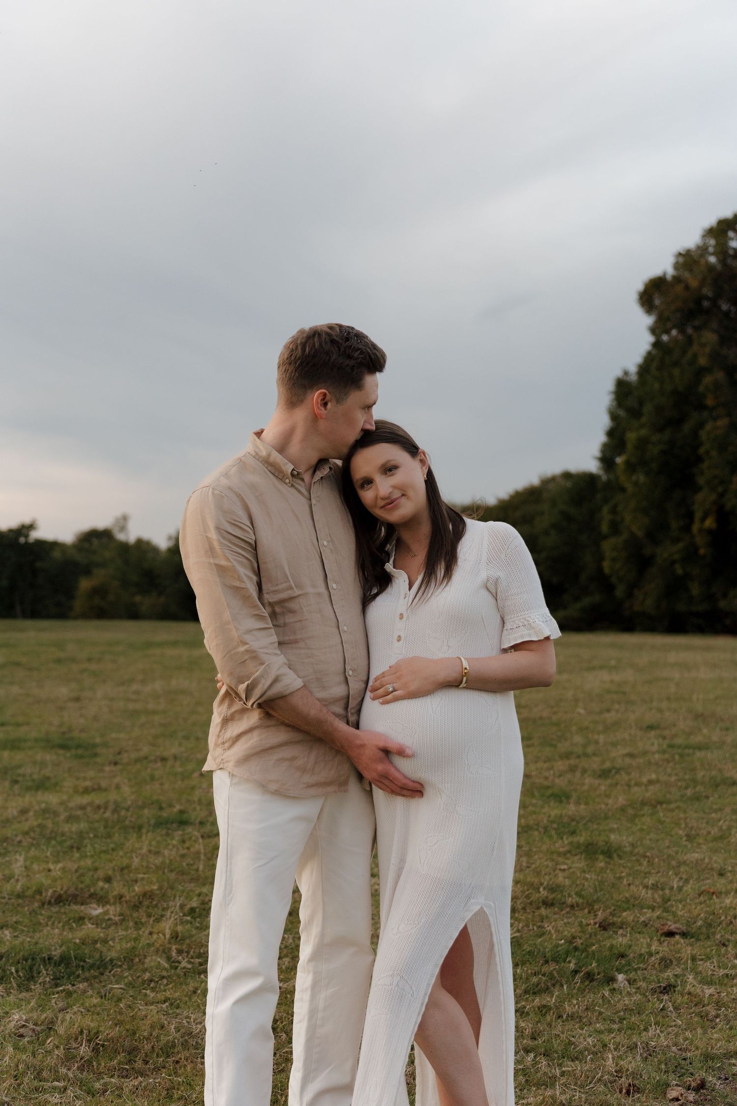 A romantic couple in white and beige outfits share an intimate moment in a pastoral setting.
