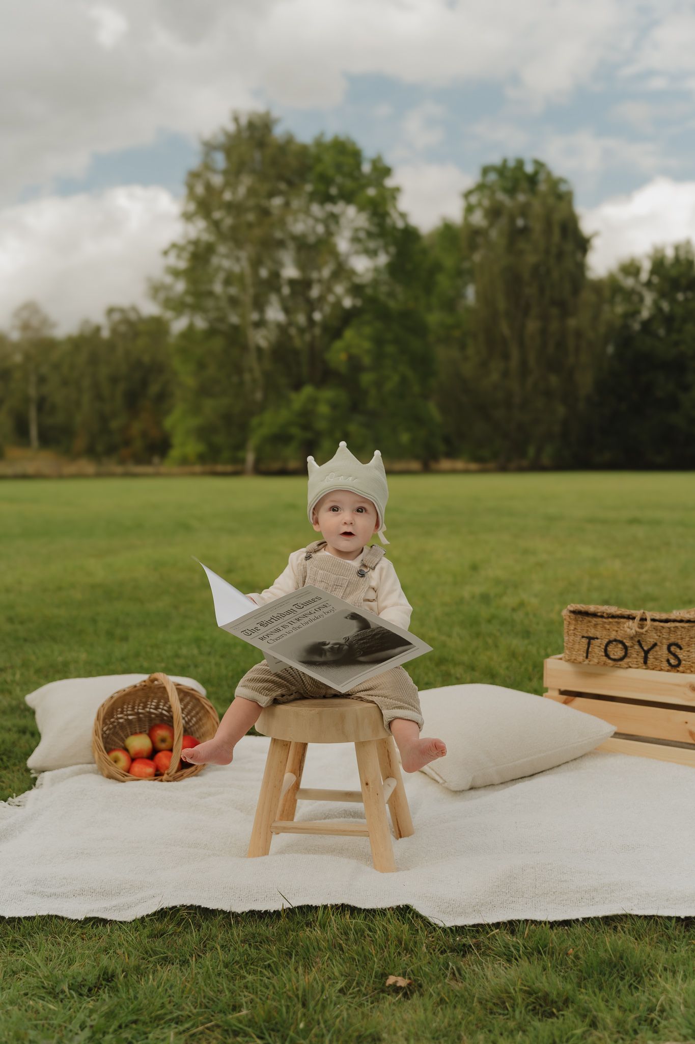 Picnic setup in grassy field with blanket, wooden stool, and basket on sunny day.