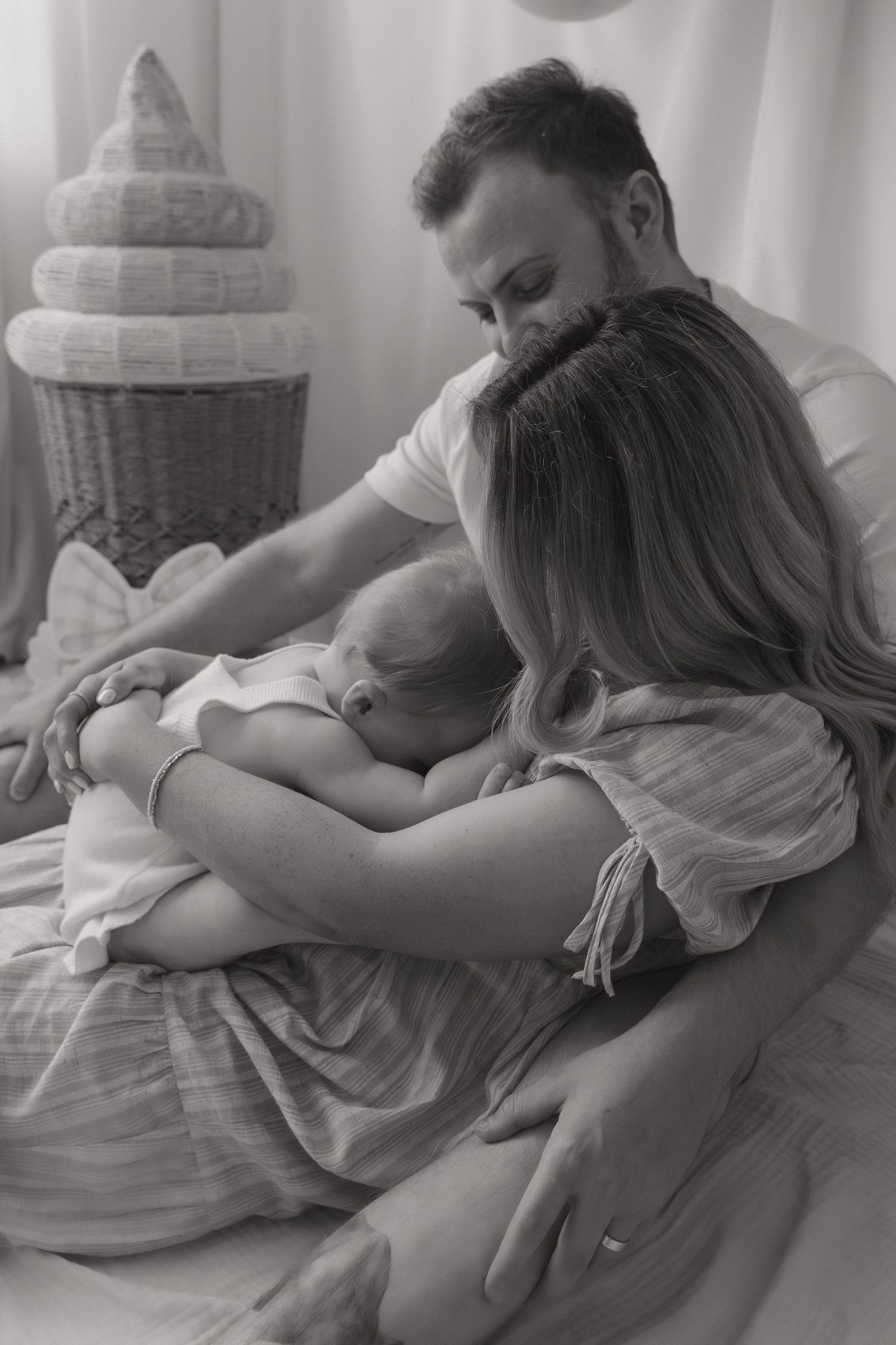 A tender black and white photograph of a family sharing an intimate moment together on a bed.