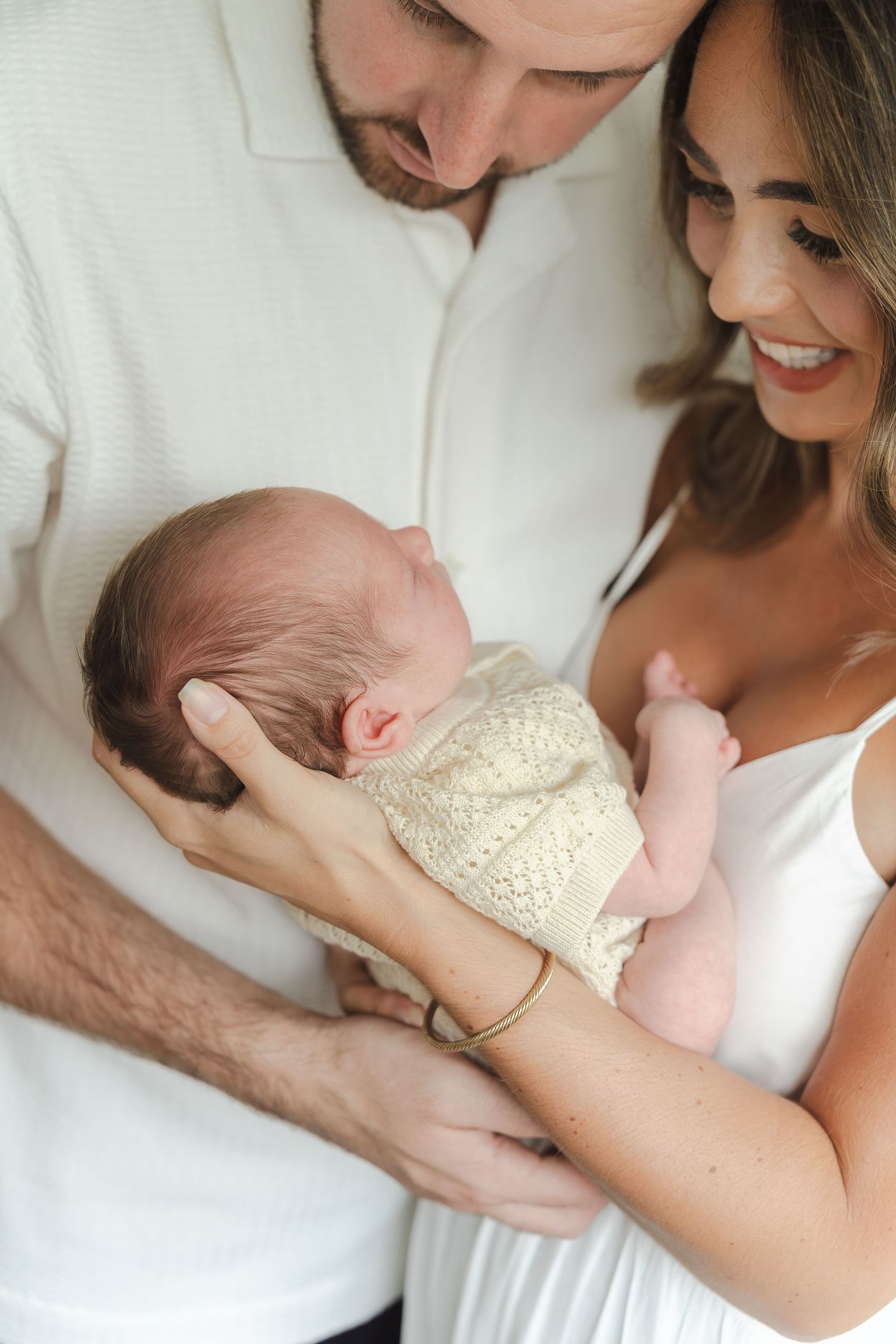 A couple in white clothing holds and gazes lovingly at their sleeping newborn baby in a series of tender moments.