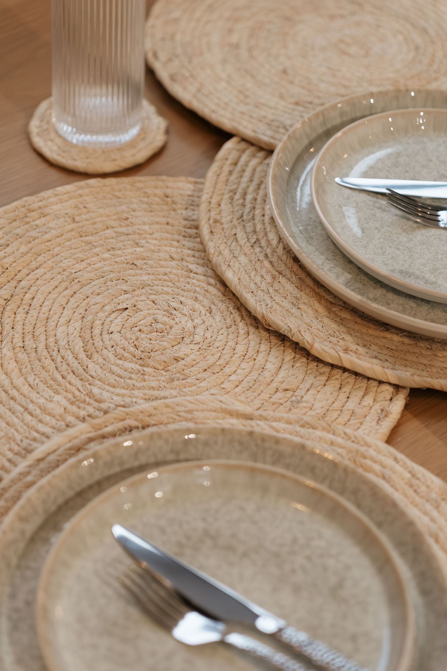 Rustic woven jute placemats with ceramic plates and silver cutlery on a wooden table.