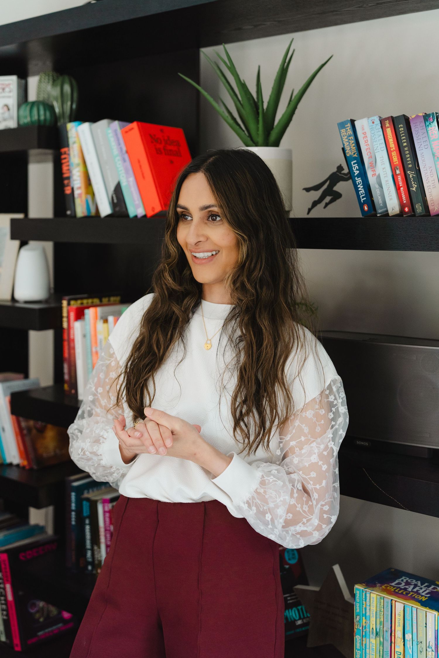 A series of photos showing someone in a white lace top and burgundy pants sitting by bookshelves in a home office.