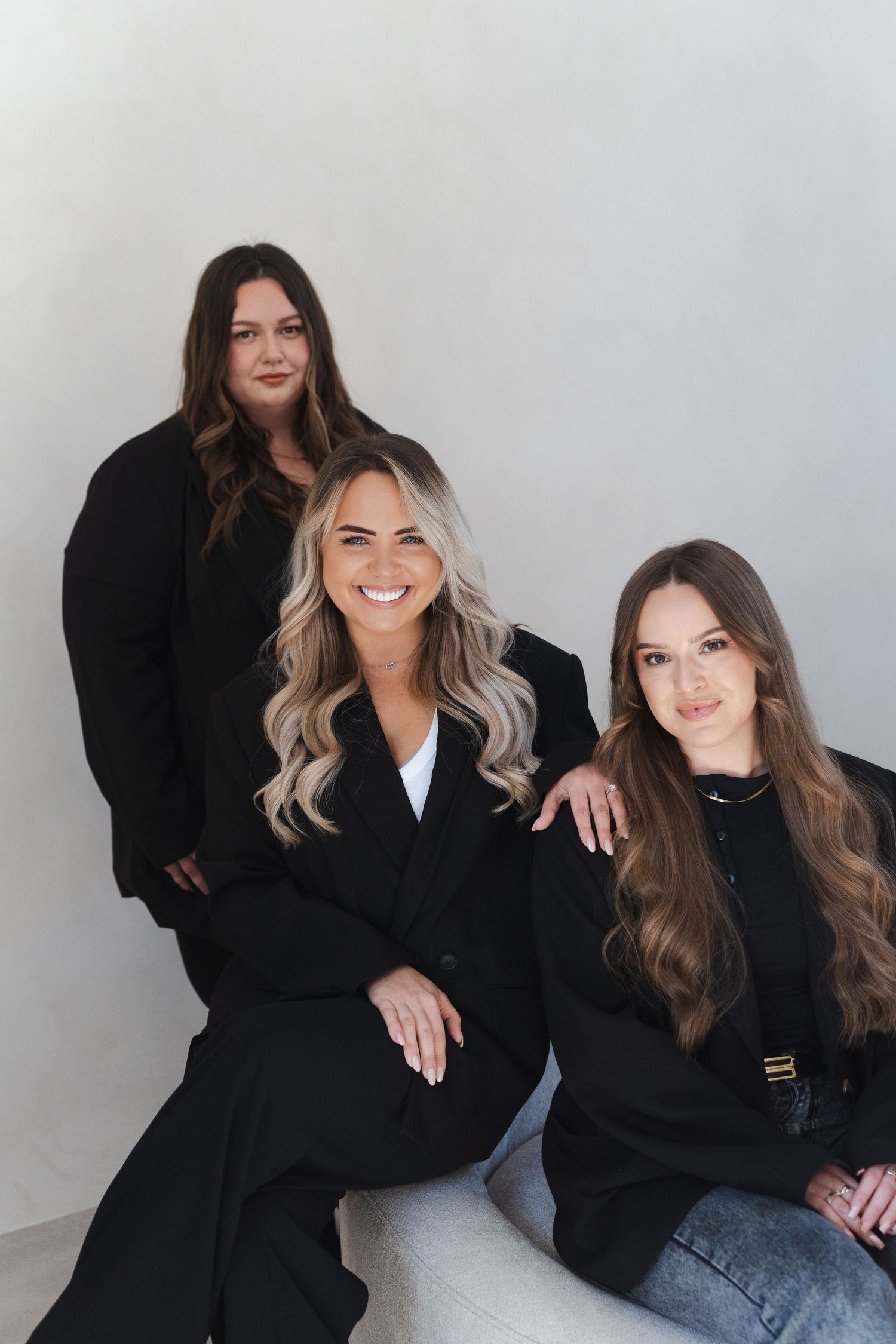 Two women in black outfits pose together against a gray background in a series of casual studio photos.